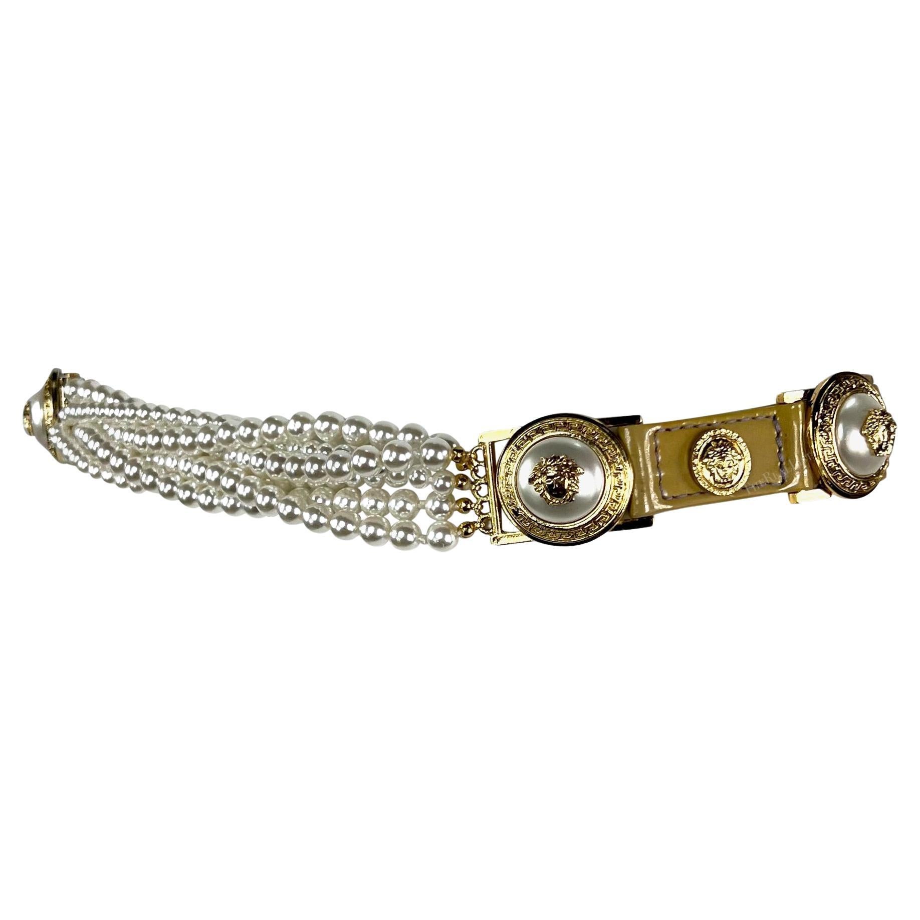  Issue de la collection automne-hiver 1994, cette ceinture chic en cuir verni beige de Gianni Versace présente des lanières en cuir verni beige ornées d'emblèmes de la Méduse de Versace en or et en fausses perles sur l'ensemble de la ceinture.