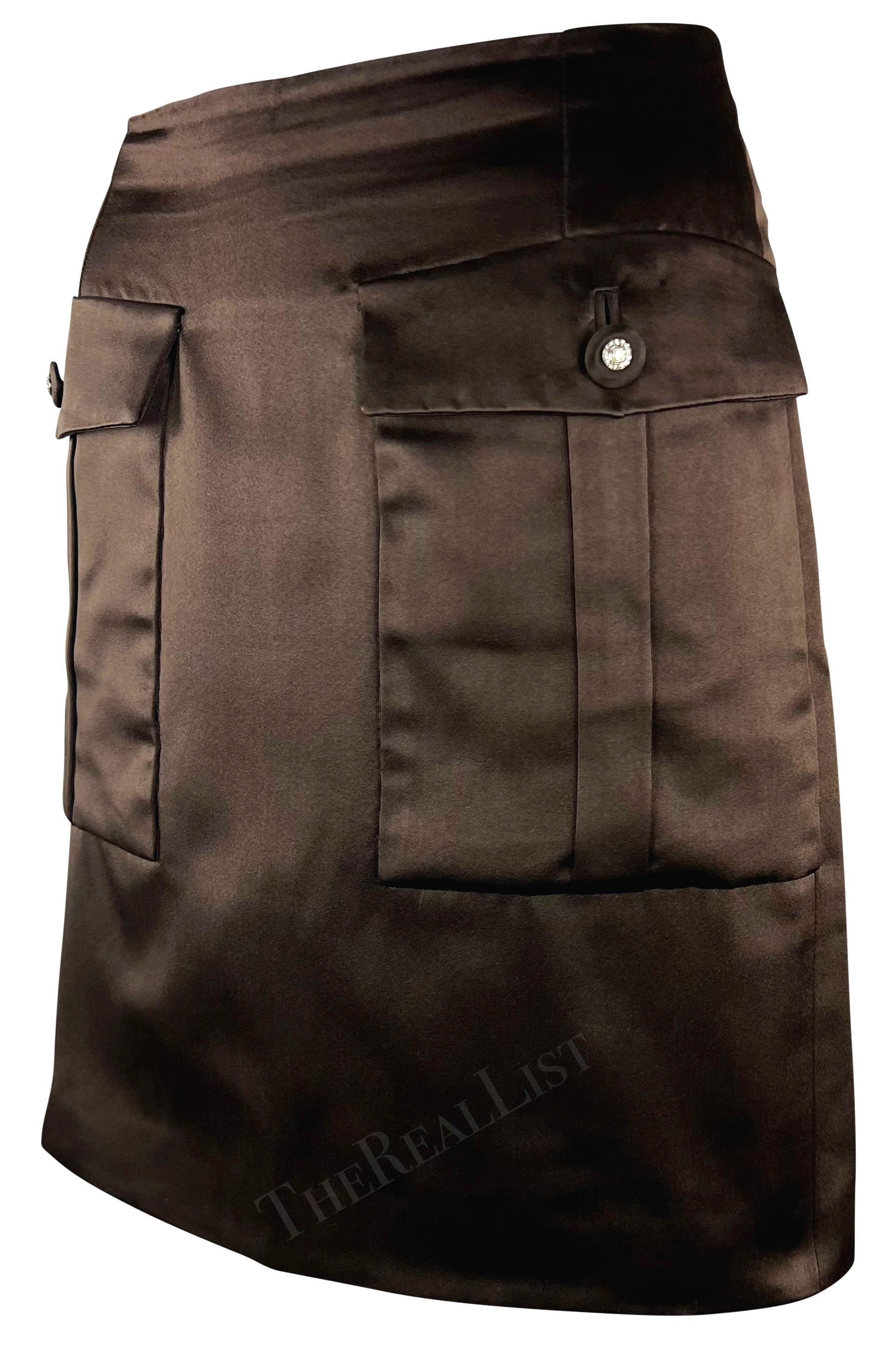Ti presentiamo una favolosa gonna corta in raso marrone di Gianni Versace, disegnata da  Gianni Versace per la collezione Autunno/Inverno 1996. Questa elegante gonna in seta, realizzata interamente in raso marrone, presenta due ampie tasche con