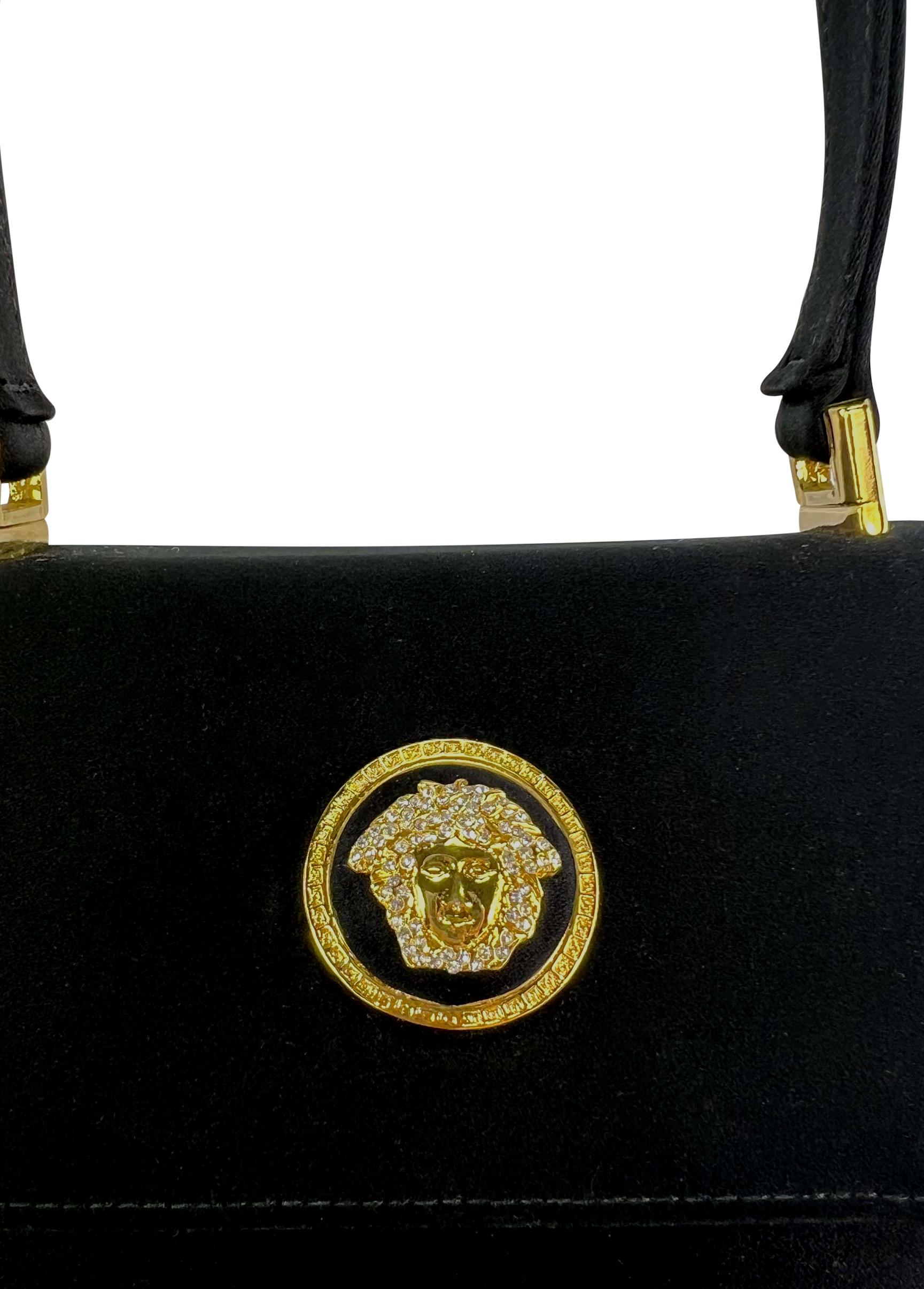 Gianni Versace diseñó este pequeño bolso de asa superior de satén negro para su Colección Otoño/Invierno 1996. Con un cierre de solapa adornado con un relieve de Medusa cubierto de pedrería, este mini bolso se completa con una bandolera extraíble