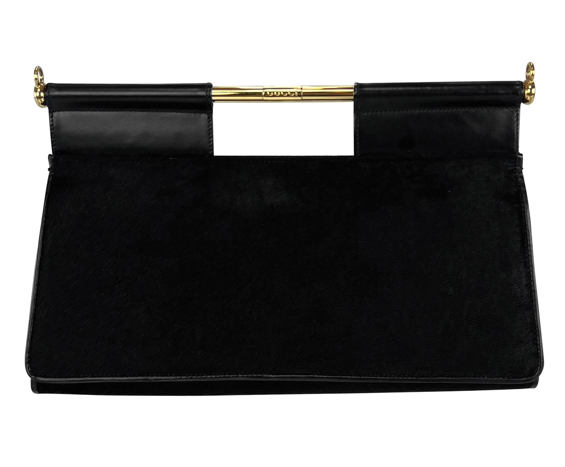 This Gucci by Tom Ford crossbody bag from Fall/Winter 1996 is crafted from black pony hair style cowhide with a sleek, triangular structure. Featuring a gold-tone engraved bar closure, leather trim, and a detachable strap, it transitions seamlessly