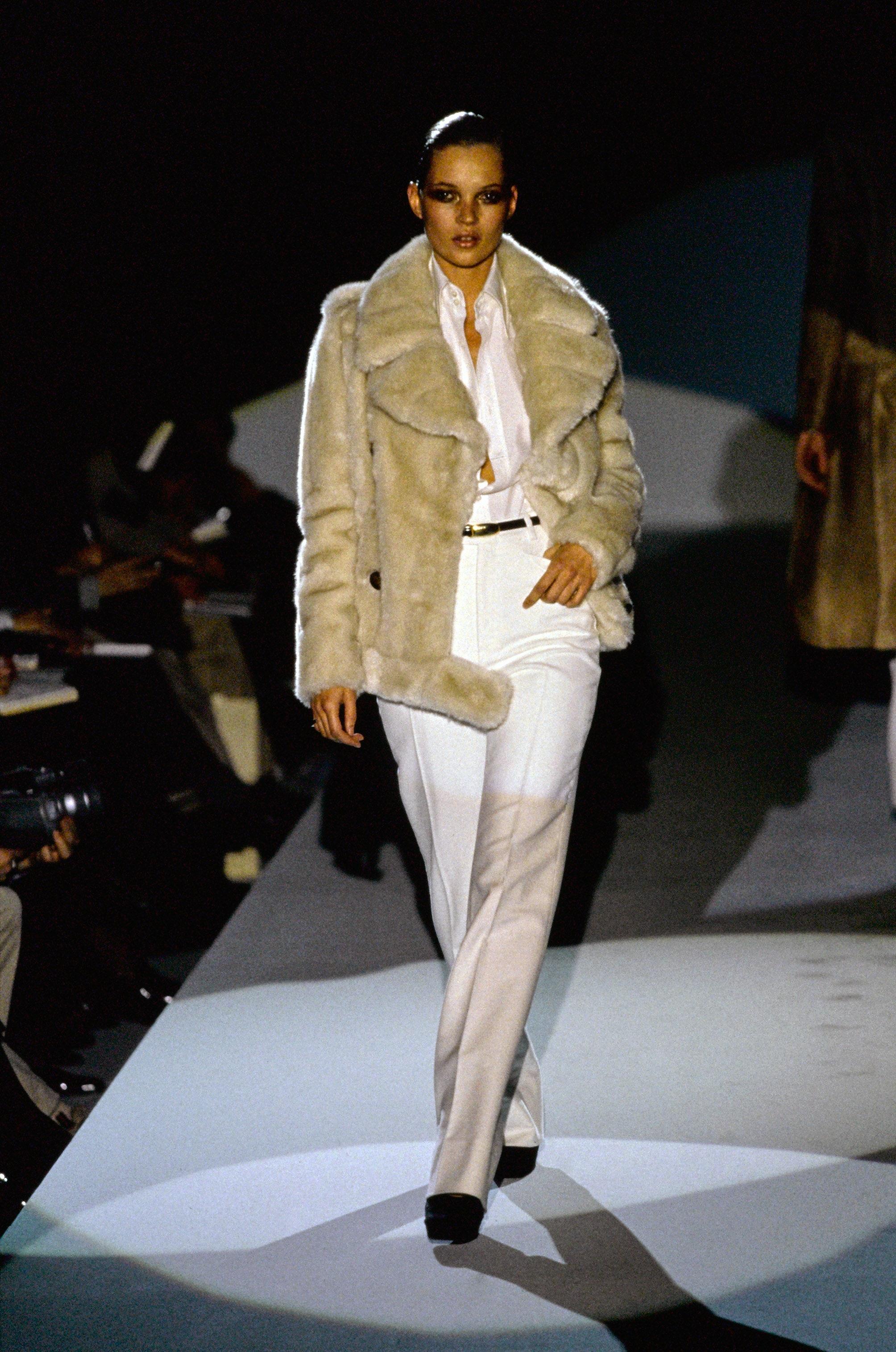 TheRealList presents: a cream faux fur double-breasted Gucci jacket with a large peak lapel and collar, designed by Tom Ford. This coat was debuted on the F/W 1996 runway in look 28 and was modeled by Kate Moss. This oversized coat features fleecy