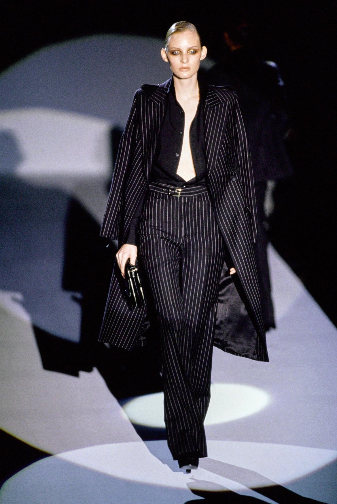 TheRealList presents: an iconic black pinstripe Gucci trench coat, designed by Tom Ford. From the Fall/Winter 1996 collection, this coat debuted as part of look 18 modeled by Amy Wesson, and was also featured in the season's ad campaign. This