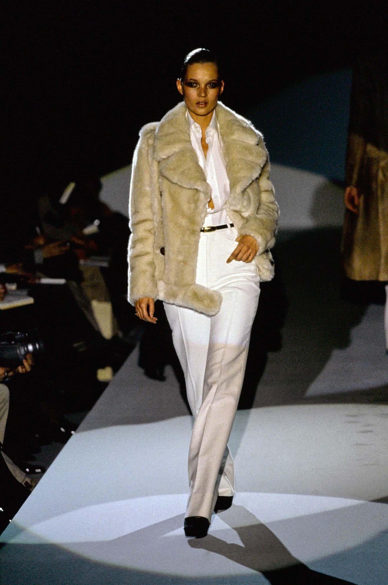 Présentation d'une veste Gucci à double boutonnage en fausse fourrure marron, avec un large revers et un col en pointe, conçue par Tom Ford. La version beige de ce manteau a fait ses débuts sur le défilé de l'automne-hiver 1996 sur le look 28 de