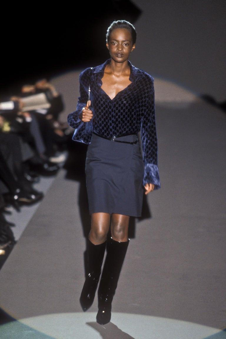 Issue de la collection automne/hiver 1997 de Gucci sous la direction de Tom Ford, cette jupe portefeuille à rayures marines présente une taille asymétrique et des bordures en cuir verni brillant. Doté d'une boucle 