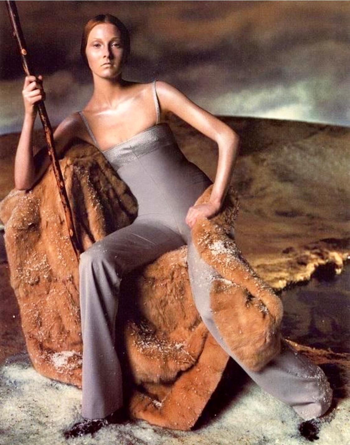 Presenta una tuta borchiata di Gianni Versace, disegnata da Donatella Versace. Dalla collezione Autunno/Inverno 1998, la versione argentata di questa tuta è apparsa nella campagna pubblicitaria della stagione, fotografata da Steven Meisel, e in