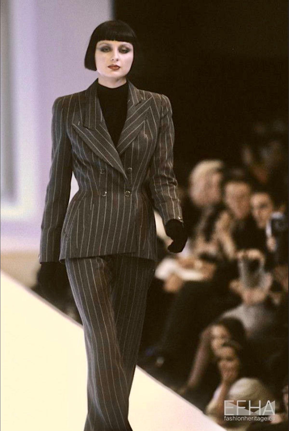 Presenting a striking dark green power suit designed by Manfred Thierry Mugler for his Fall/Winter 1998 collection, with a similar suit debuting on the season's runway. The jacket features an oversized peak lapel and a double-breasted snap closure.