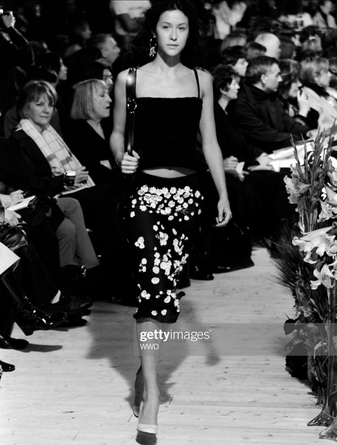 Presenting a beautiful sheer black flower-accented Dolce and Gabbana skirt. From the Fall/Winter 1999 collection and covered in fabric daisy appliqués, this fabulous skirt debuted on the season's runway on Natane Boudreau and features a slit on one