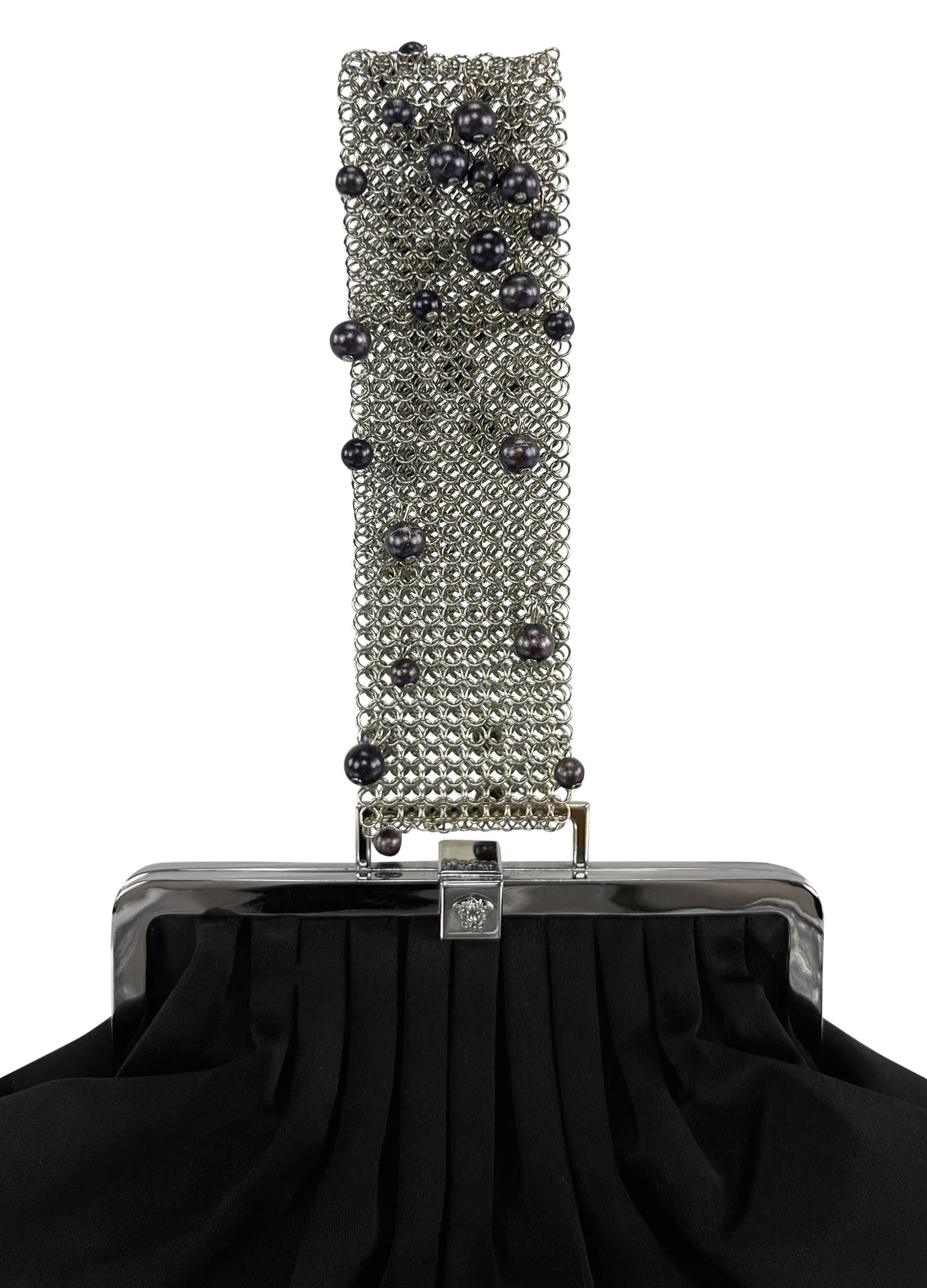 Donatella Versace designed this elegant black satin evening bag for the Gianni Versace Fall/Winter 1999 collection. This chic bag is constructed of black satin and features a silver-tone clamshell design. The bag is elevated with black faux pearls