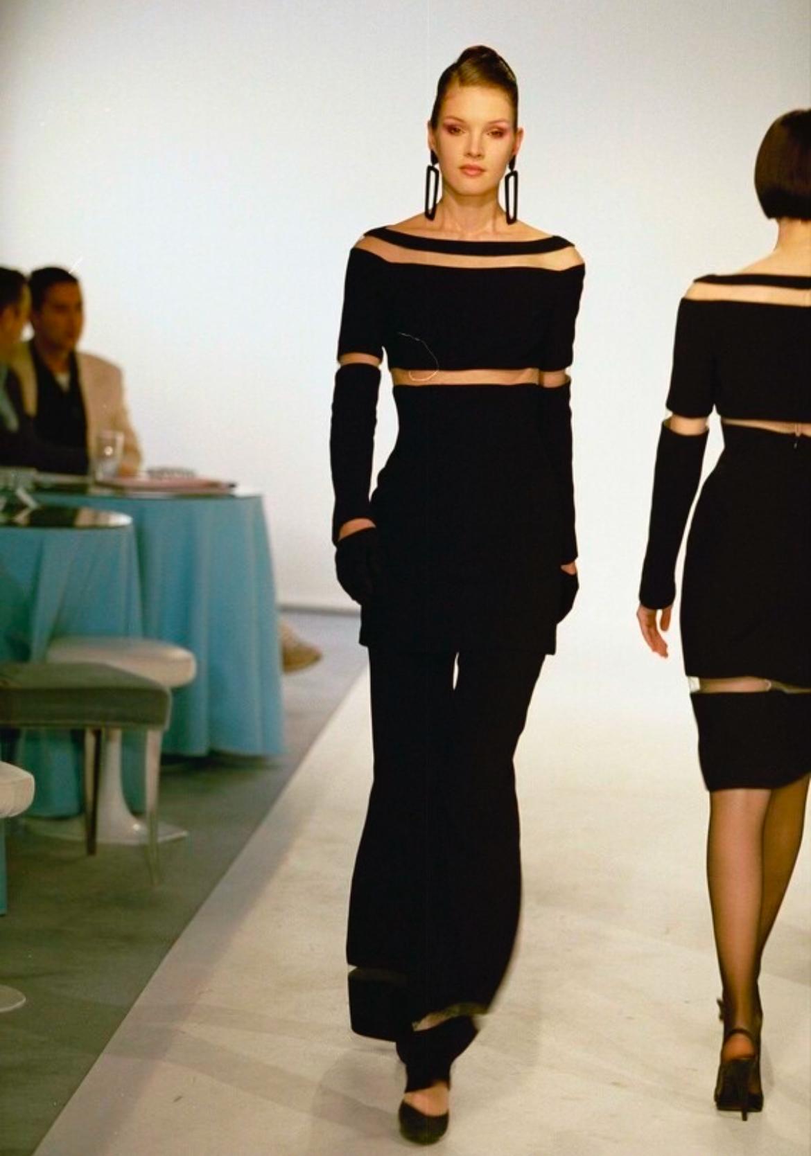 From Thierry Mugler’s Fall/Winter 1999 collection, this two-piece black pantsuit features a fitted tunic top and high-waisted flared trousers. The set is accented with bold, strategically placed beige mesh panels at the neckline, waist, sleeves, and