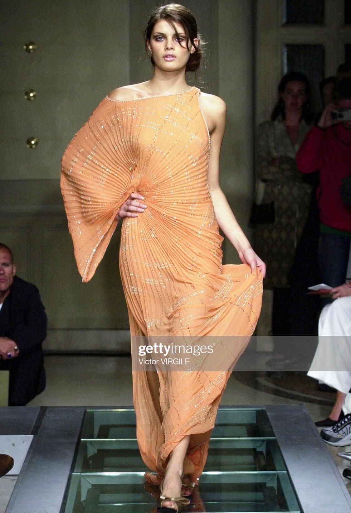 Présentation d'une robe de Gianni Versace conçue pour une déesse romaine/précienne moderne, dessinée par Donatella Versace pour la collection automne/hiver 2000. Cette robe est construite en soie plissée, qui s'ajuste à la hanche. Cette robe se