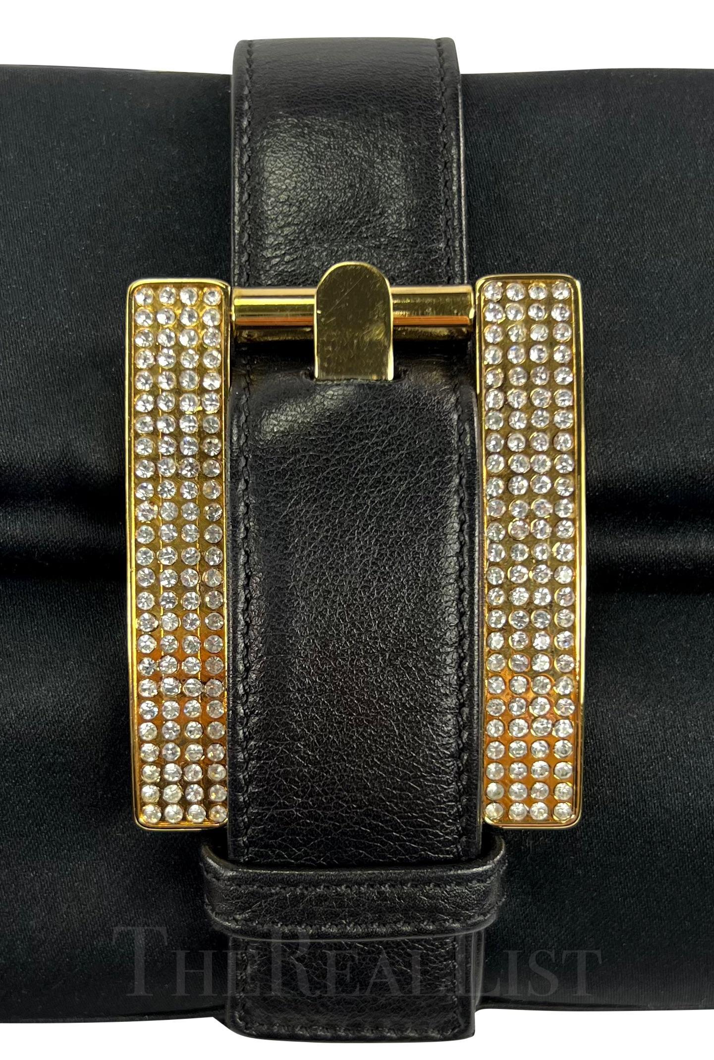 Ti presentiamo un'elegante borsa a tracolla in raso nero di Gianni Versace, disegnata da Donatella Versace. Questa borsa, appartenente alla collezione Autunno/Inverno 2001, ha la stessa forma della fibbia che si ritrova in diversi look delle