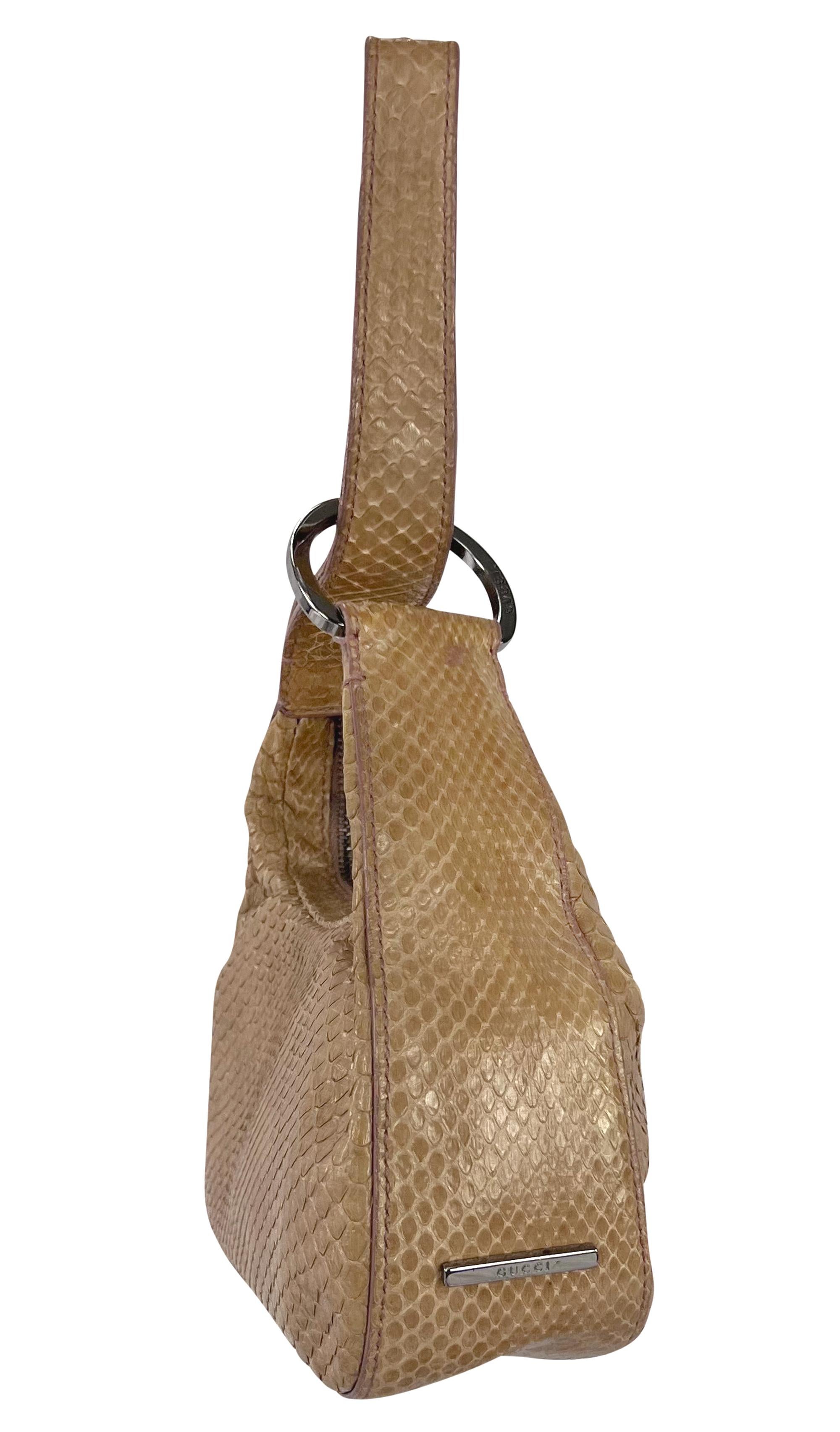 From Gucci’s Fall/Winter 2001 collection by Tom Ford, this beige snakeskin mini bag features a structured silhouette and a distinctive ring-accented wristlet strap. The design is finished with a zip-top closure and subtle silver-tone Gucci logo