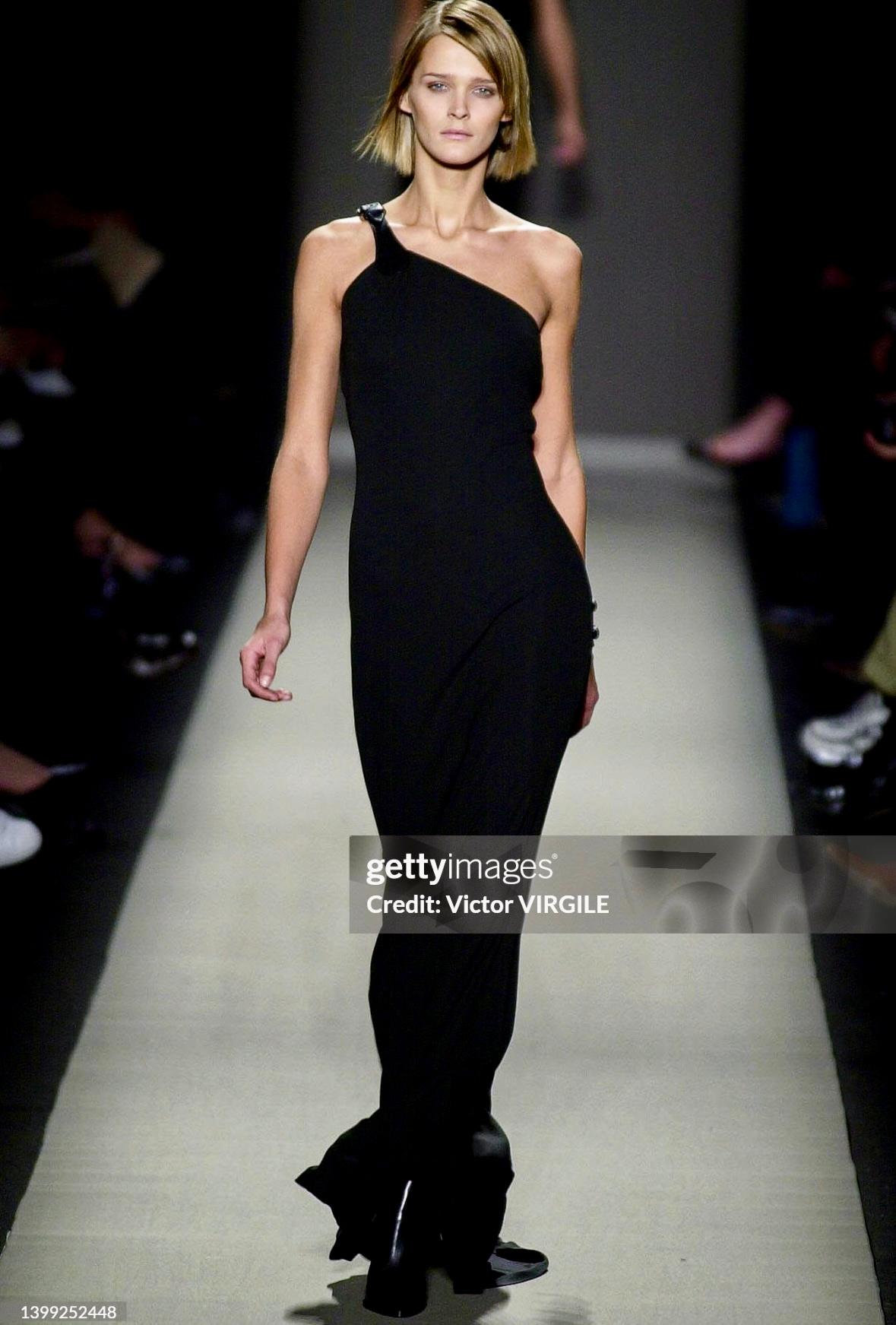 This Michael Kors black bodycon gown debuted on the Fall/Winter 2001 runway as look 84, modeled by Carmen Kass. This striking design features an leather strap with a buckle detail and a sleek, floor-length silhouette. 

Approximate
