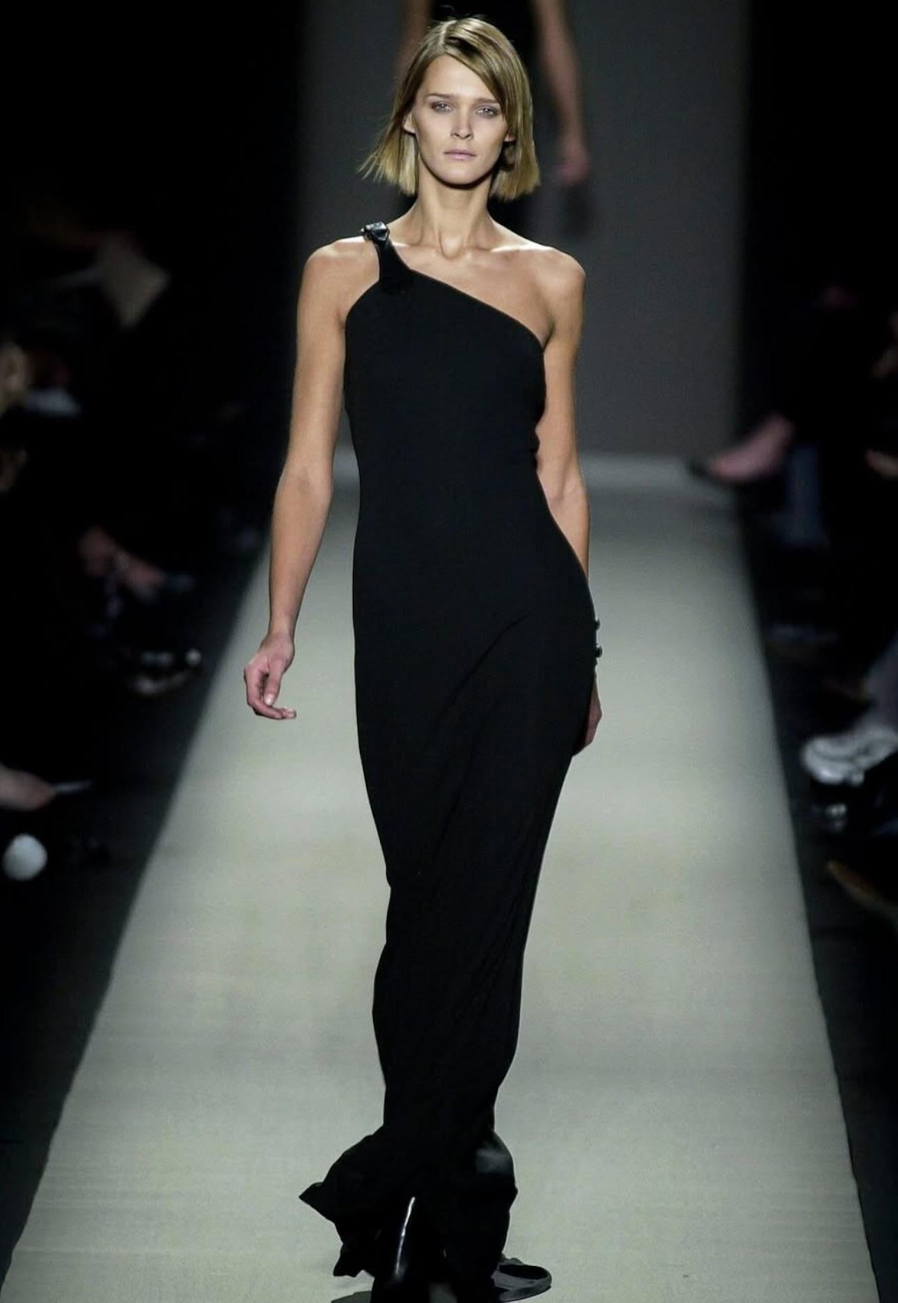 Cette robe noire bodycon Michael Kors a été présentée pour la première fois sur le défilé automne-hiver 2001, dans le look 84, par Carmen Kass. Ce modèle remarquable est doté d'une lanière en cuir avec une boucle et d'une silhouette élégante qui
