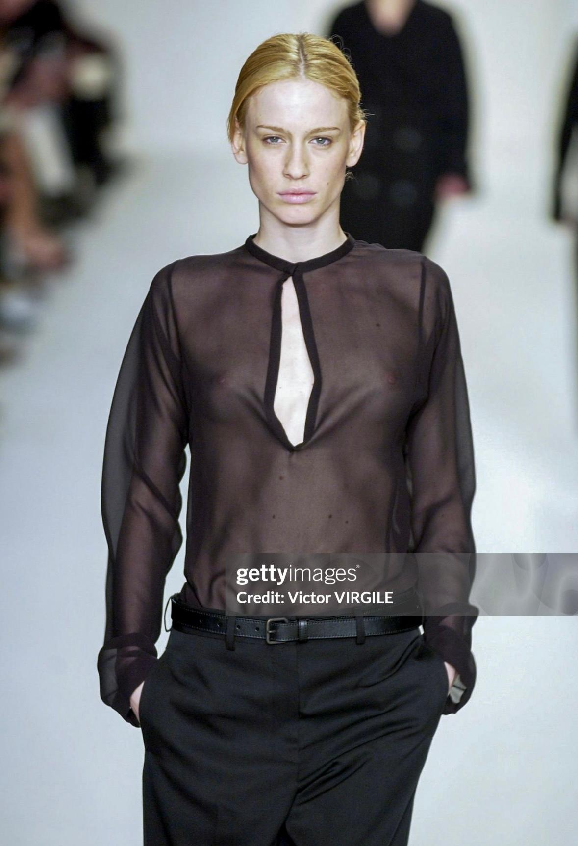 Questa camicetta tunica nera trasparente di Calvin Klein della collezione A. Winter 2002 ha debuttato sulla passerella della stagione come parte del look 15 indossato da Nataša Vojnović. Questo modello minimalista presenta una scollatura profonda e