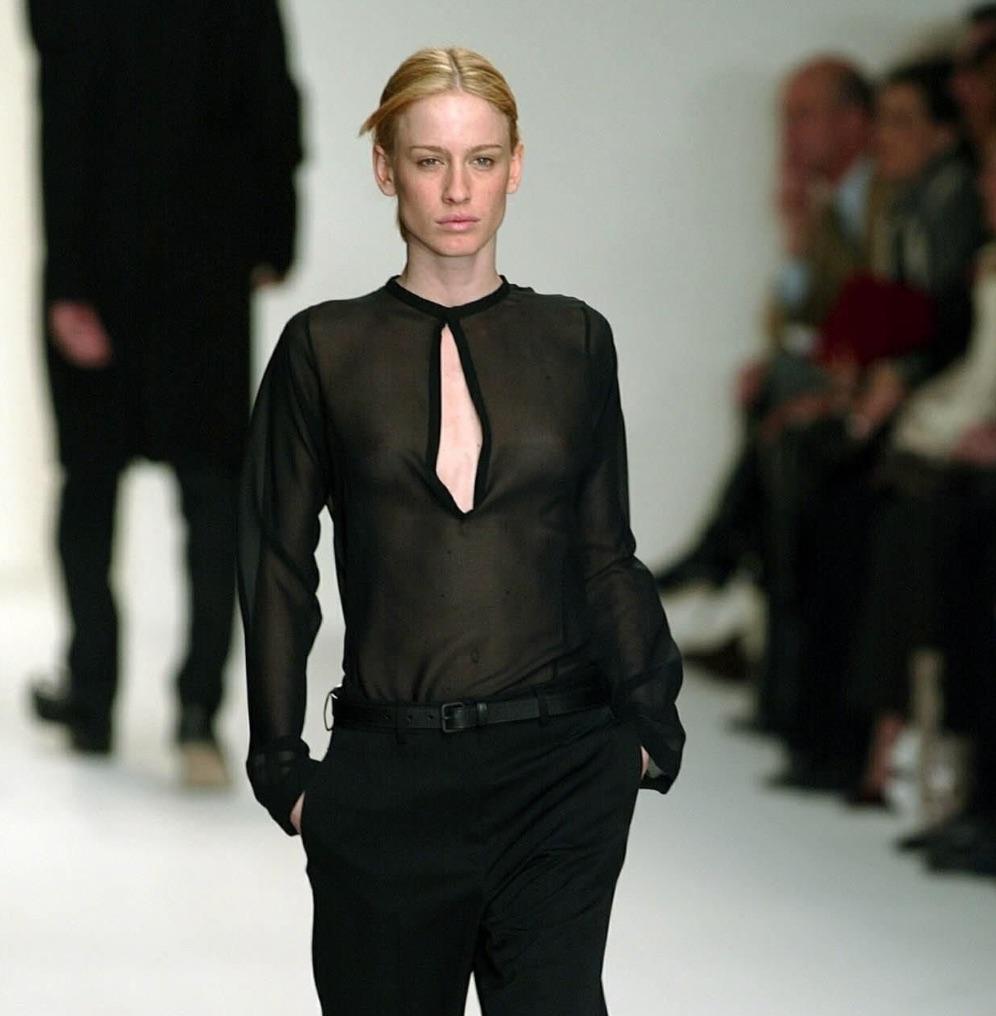Ce chemisier tunique noir transparent de Calvin Klein, issu de la collection Automne/Hiver 2002, a fait ses débuts sur le défilé de la saison dans le look 15 porté par Nataša Vojnović. Ce modèle minimaliste présente un décolleté plongeant et des