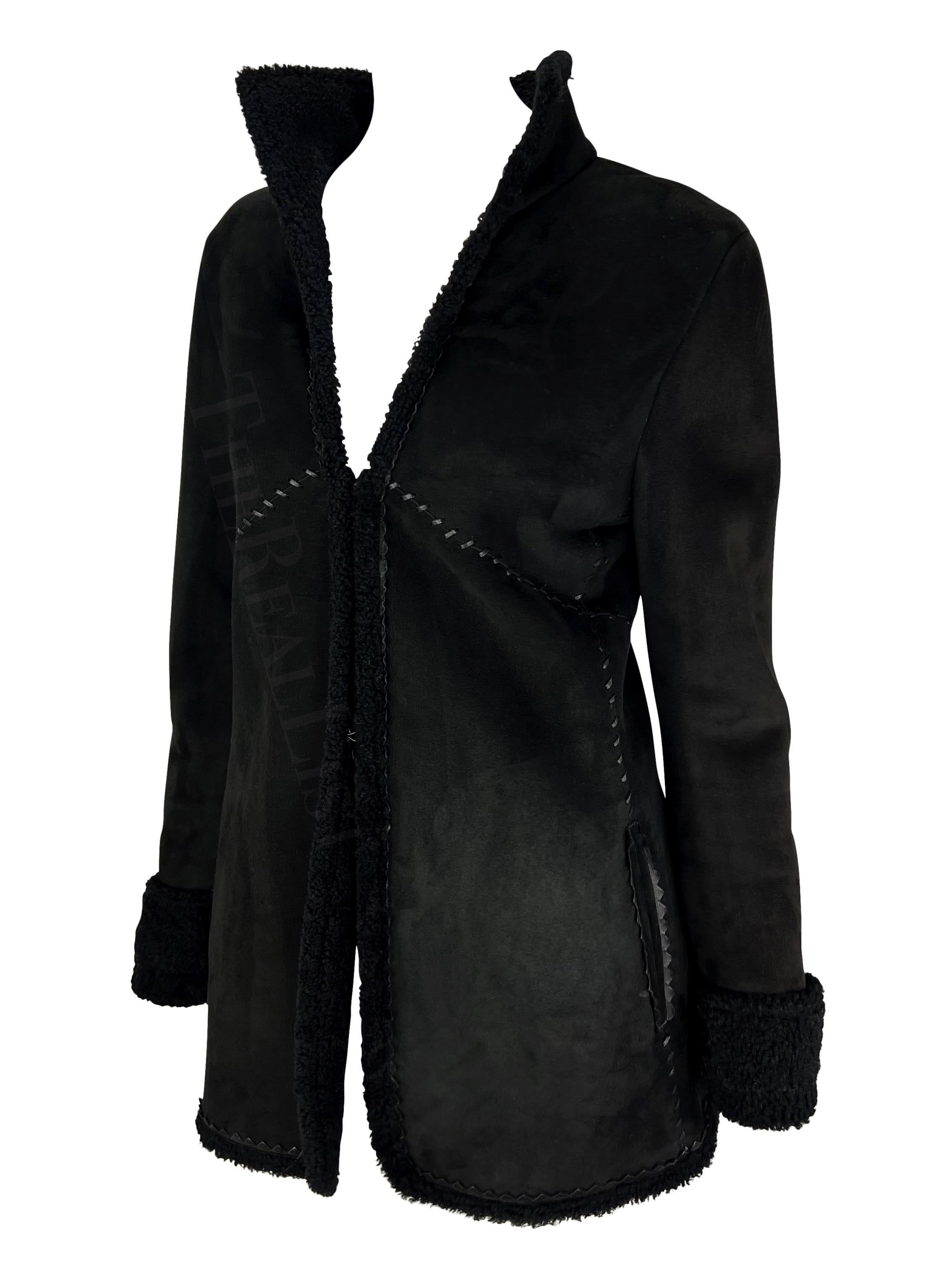 Présentation d'un manteau en shearling noir Gianni Versace, dessiné par Donatella Versace. Issu de la collection automne/hiver 2002, ce manteau présente un extérieur en daim et un intérieur en shearling. La fourrure de shearling peut être repliée
