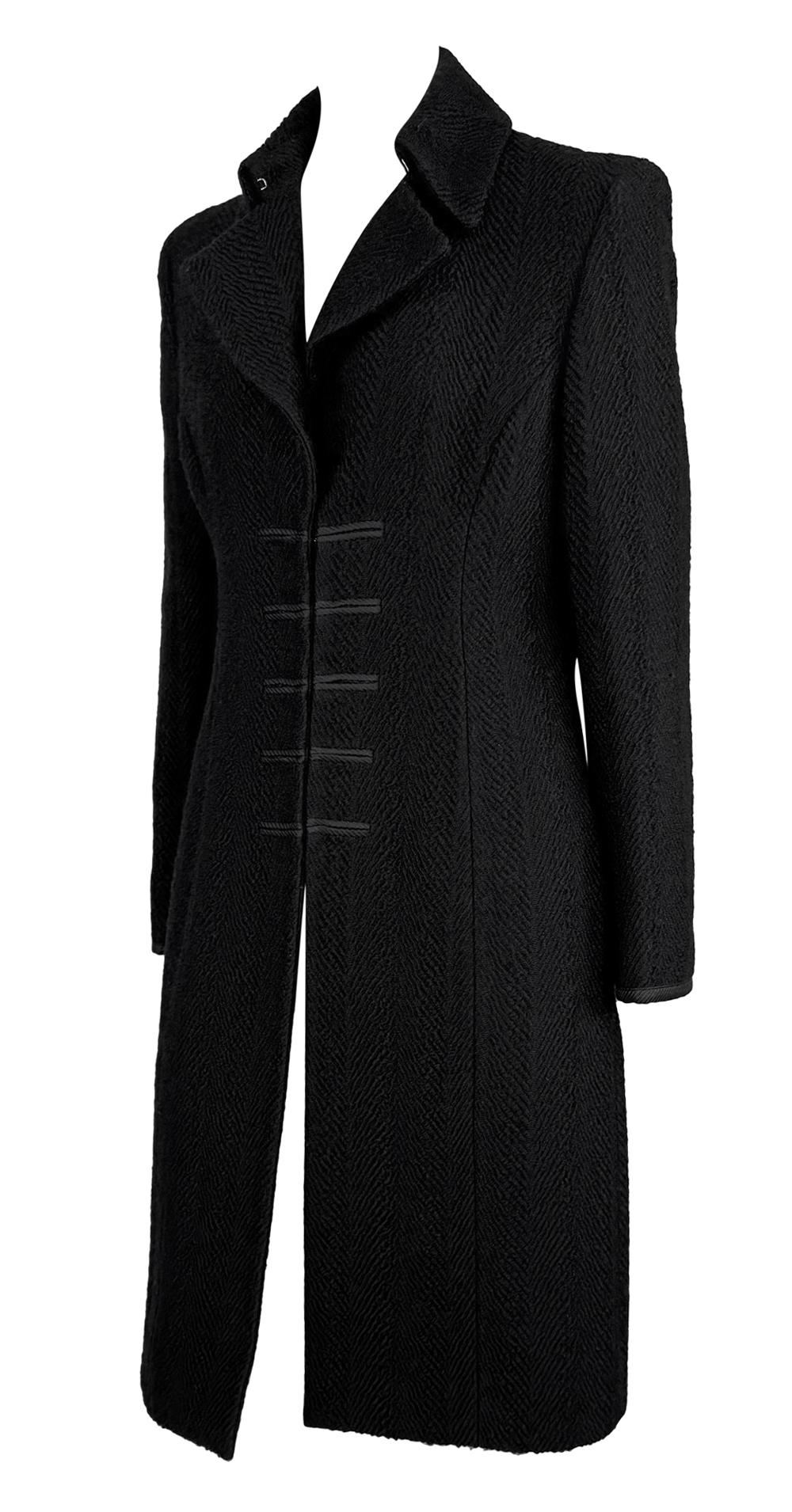 Questo trench nero di Donatella Versace for Gianni Versace è realizzato in tweed nero testurizzato. Il cappotto è caratterizzato da un bavero strutturato, chiusure con gancio e occhiello sul davanti, e un  Silhouette aderente che si allarga