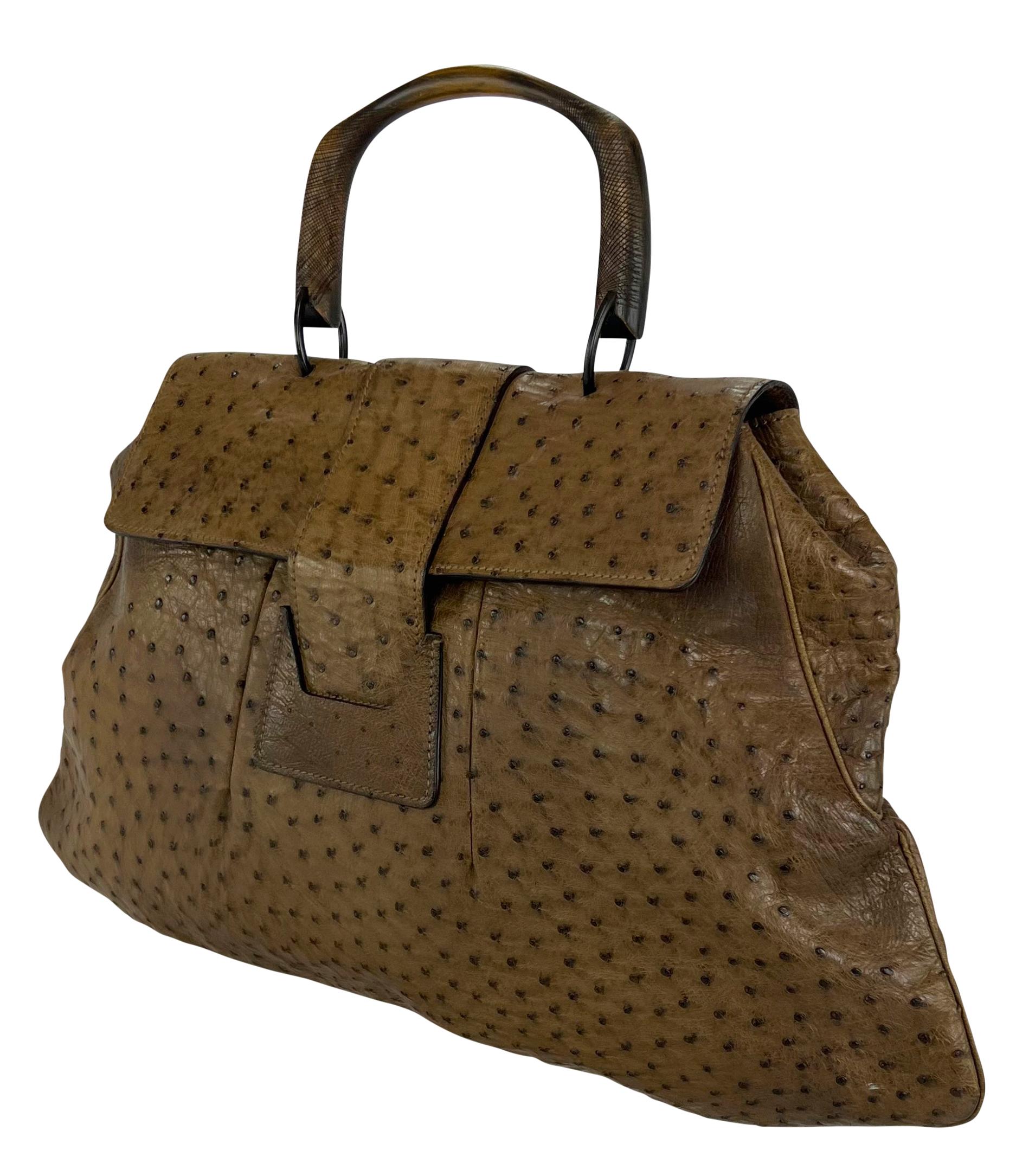 This oversized tote bag from Gucci’s Fall/Winter 2002 collection, designed by Tom Ford, is crafted from tan ostrich skin. It features a single wooden top handle and structured silhouette with a top flap closure and wide central strap detail. This