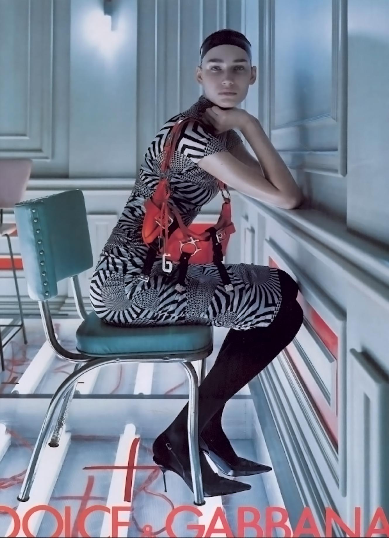 This Dolce & Gabbana dress from the Fall/Winter 2003 collection features a body-skimming silhouette in sheer black mesh with a tonal blue Op Art-inspired print. The midi-length design is ruched throughout for a sculpted fit and includes a mock neck