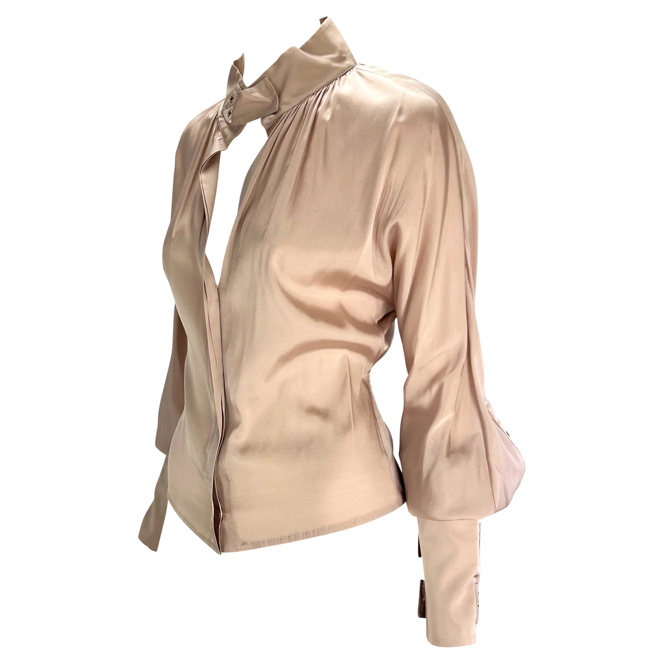 This beige silk long-sleeve Gucci top, designed by Tom Ford for the Fall/Winter 2003 collection, features luxurious silk with grommet and strap accents. The top has long cuffs with strap closures leading to voluminous sleeves. A matching strap is