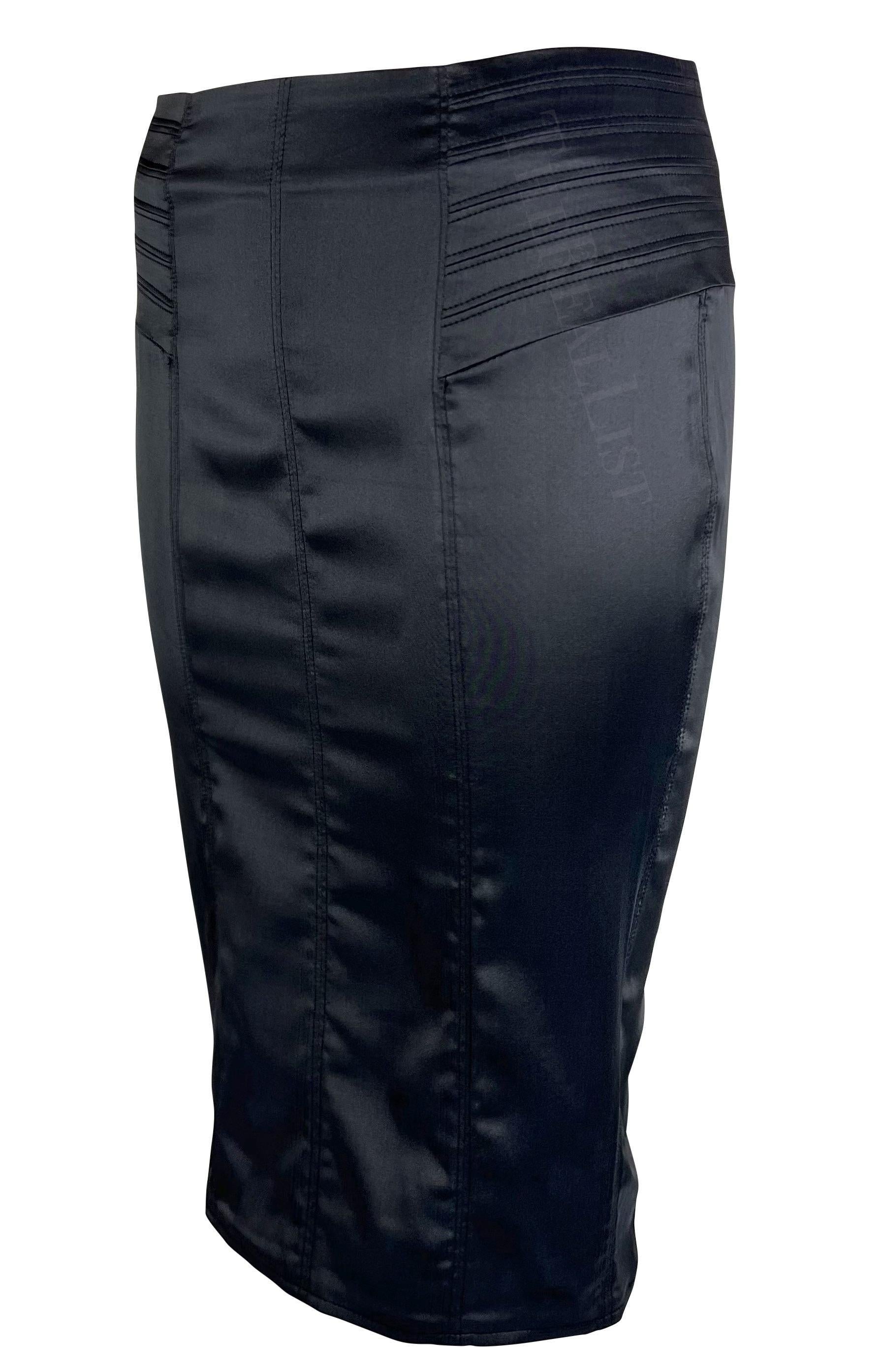 Je vous présente une fabuleuse jupe crayon Gucci en satin de soie noir, créée par Tom Ford. Issue de la collection automne-hiver 2003, cette jupe présente de larges pans et une fente dans le dos. Elle est complétée par des détails matelassés de part