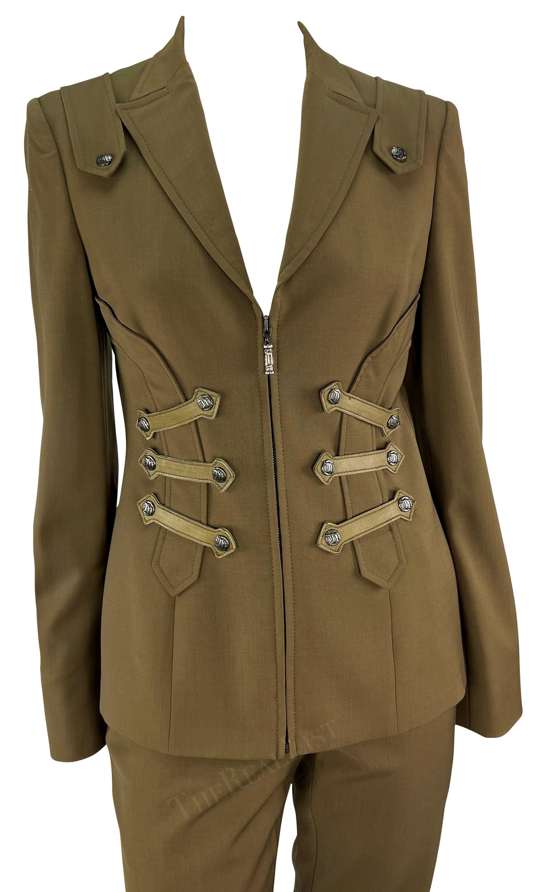 Dalla collezione Autunno/Inverno 2003, questo tailleur pantalone Versace verde oliva, disegnato da Donatella Versace, è composto da una giacca e da un pantalone coordinato con inserti in pelle. La giacca presenta una scollatura profonda, una