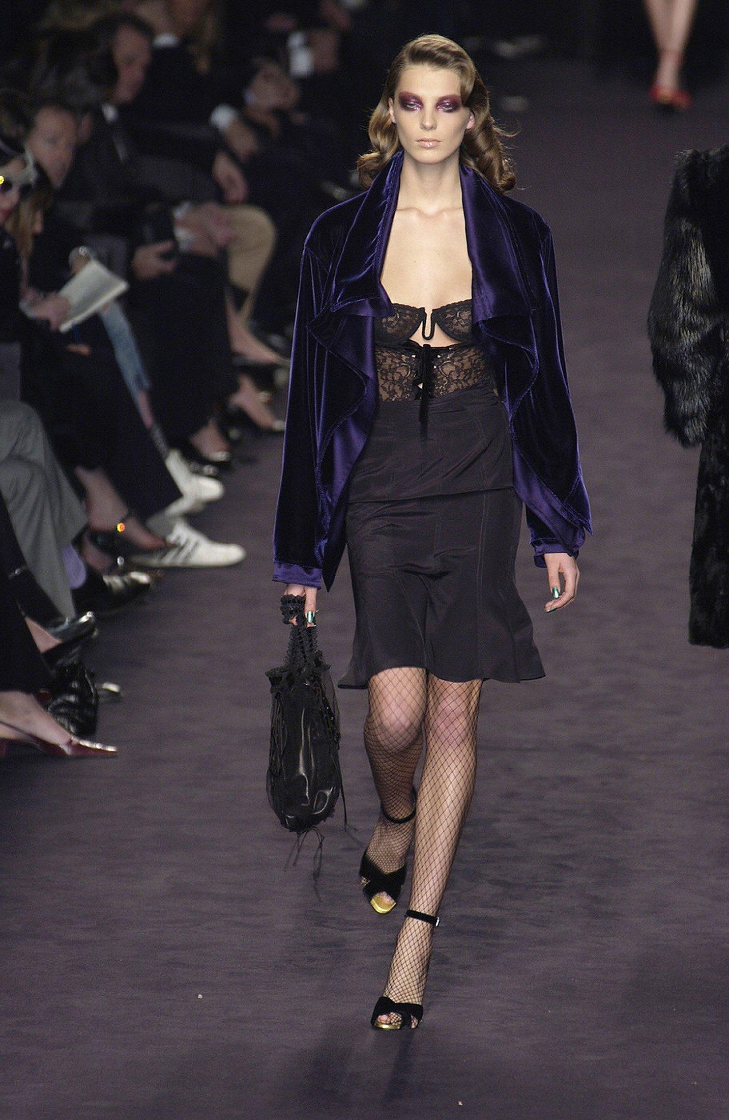This Fall/Winter 2003 Yves Saint Laurent bodysuit by Tom Ford is crafted from sheer black lace with floral motifs and delicate velvet polka dots. The dramatic plunge front is accented by a lace-up detail, framed by structured cups with ruffle trim.