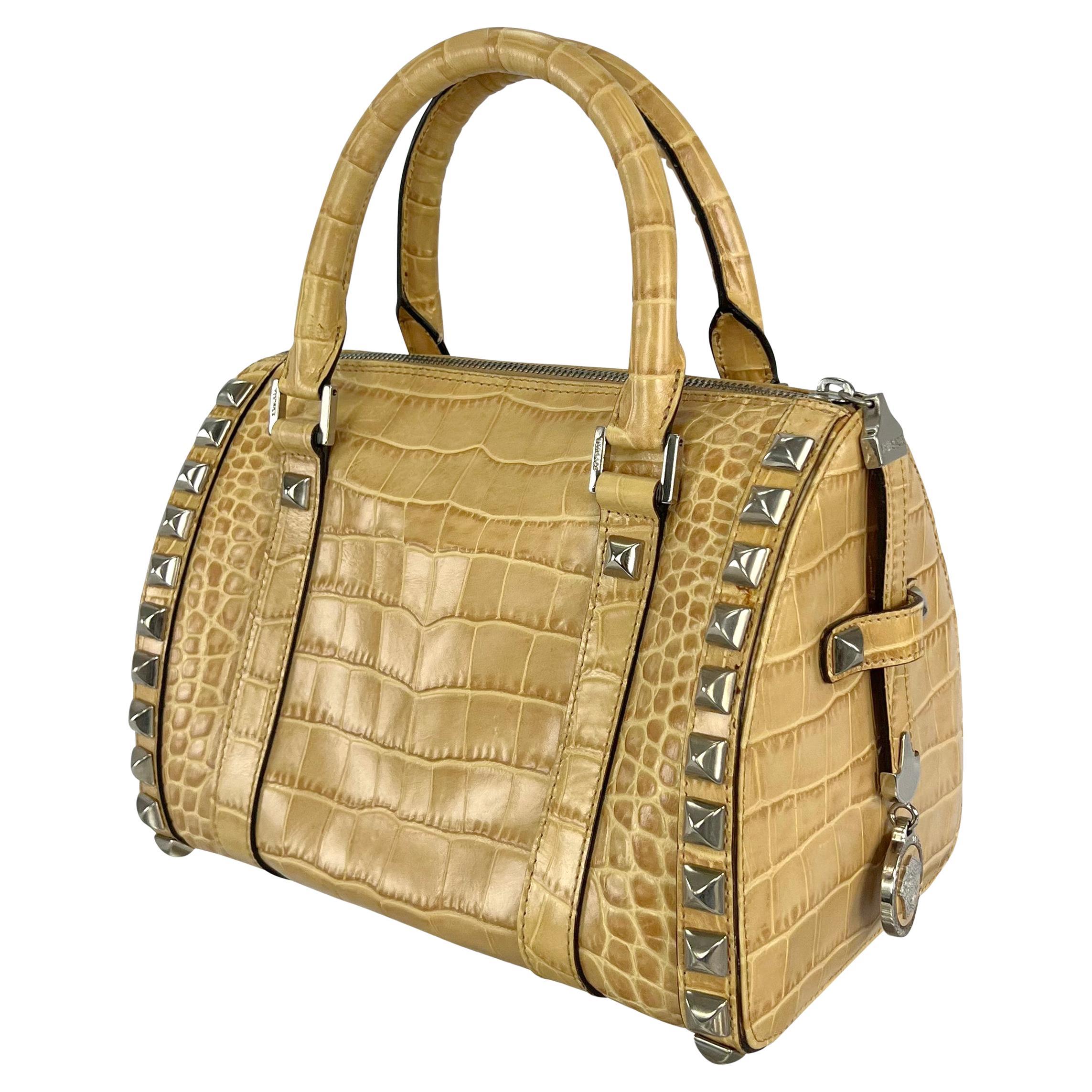 Disegnata da Donatella Versace per la collezione Autunno/Inverno 2004, questa elegante borsa beige in stile Boston presenta un sorprendente motivo a coccodrillo in rilievo. La borsa è impreziosita da borchie a piramide in tonalità argento che