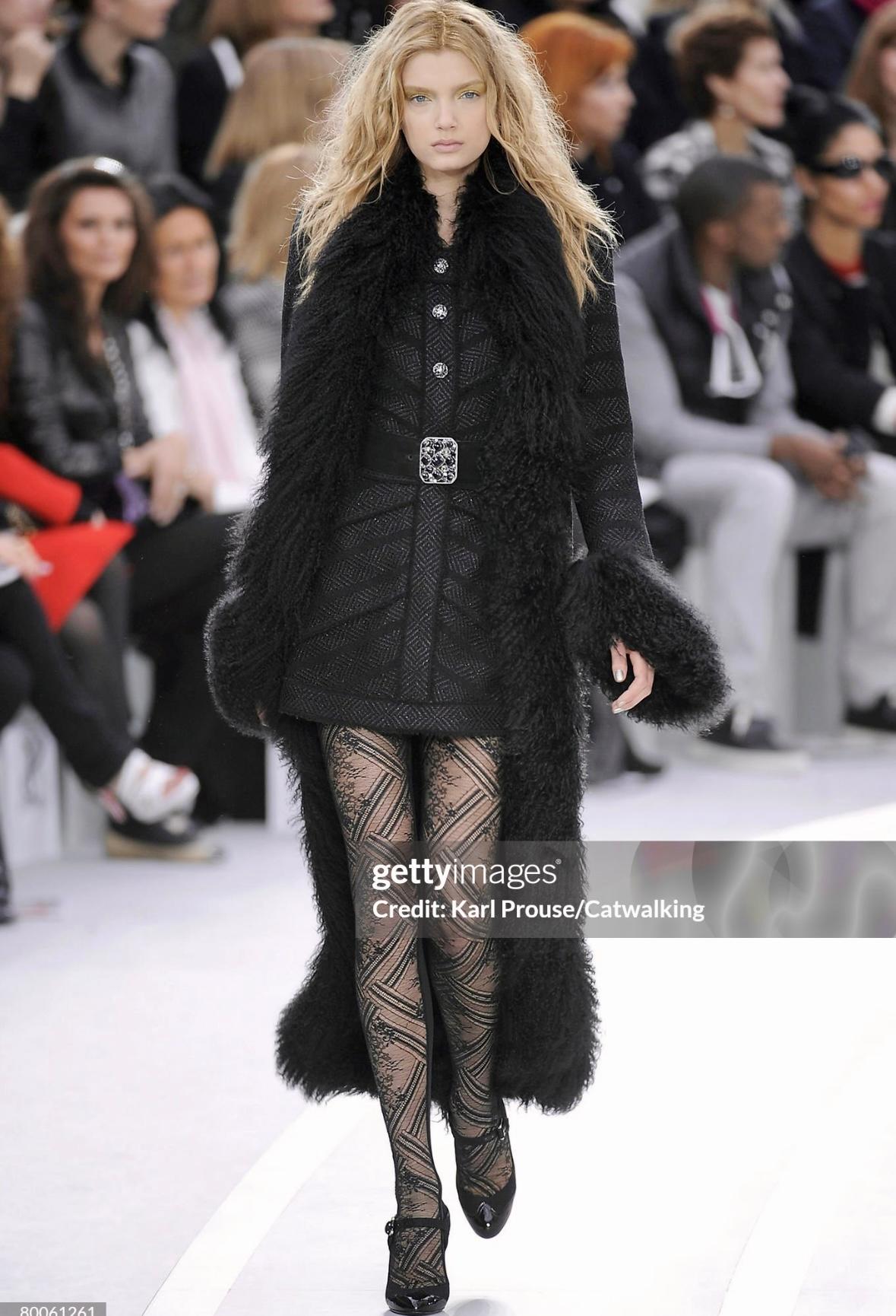 This Chanel black metallic tweed coat from Fall/Winter 2008, designed by Karl Lagerfeld, features dramatic Mongolian lamb fur trim. Seen as look 28 on the runway, the textured design blends classic Chanel tweed with bold, luxurious accents, creating
