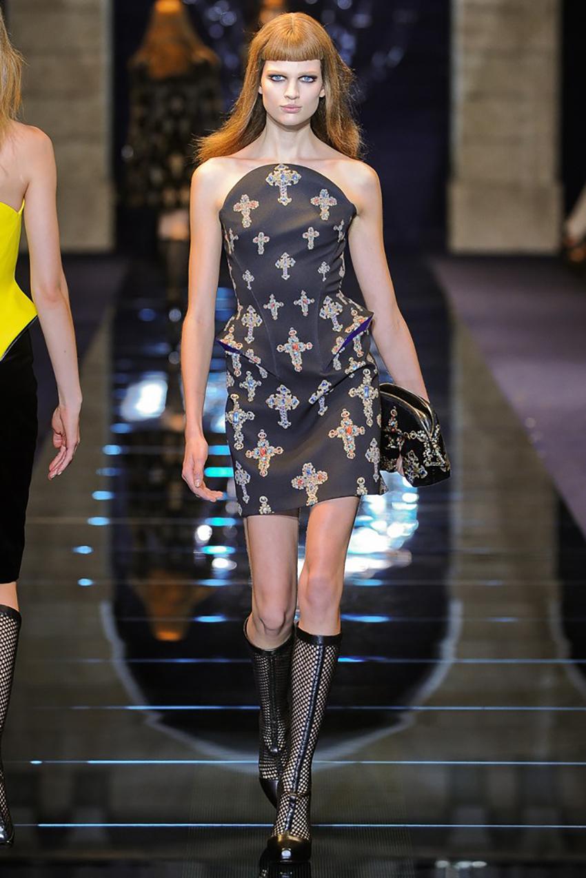Versace 
Crepe Printed Original Dress made in a pattern of studded crosses on a black background. 
It has a waisted and tight modeling along the body with hip detail in blue leather, structured by fins, strapless neckline and an invisible zipper