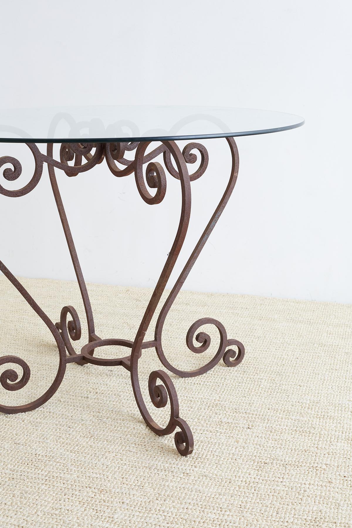 Elegant scrolled wrought iron breakfast table or patio garden table featuring four large S scrolls. Conjoined on top and bottom with scrolls on top and a ring stretcher on bottom. Each leg has a small scrolled foot. The table is constructed from