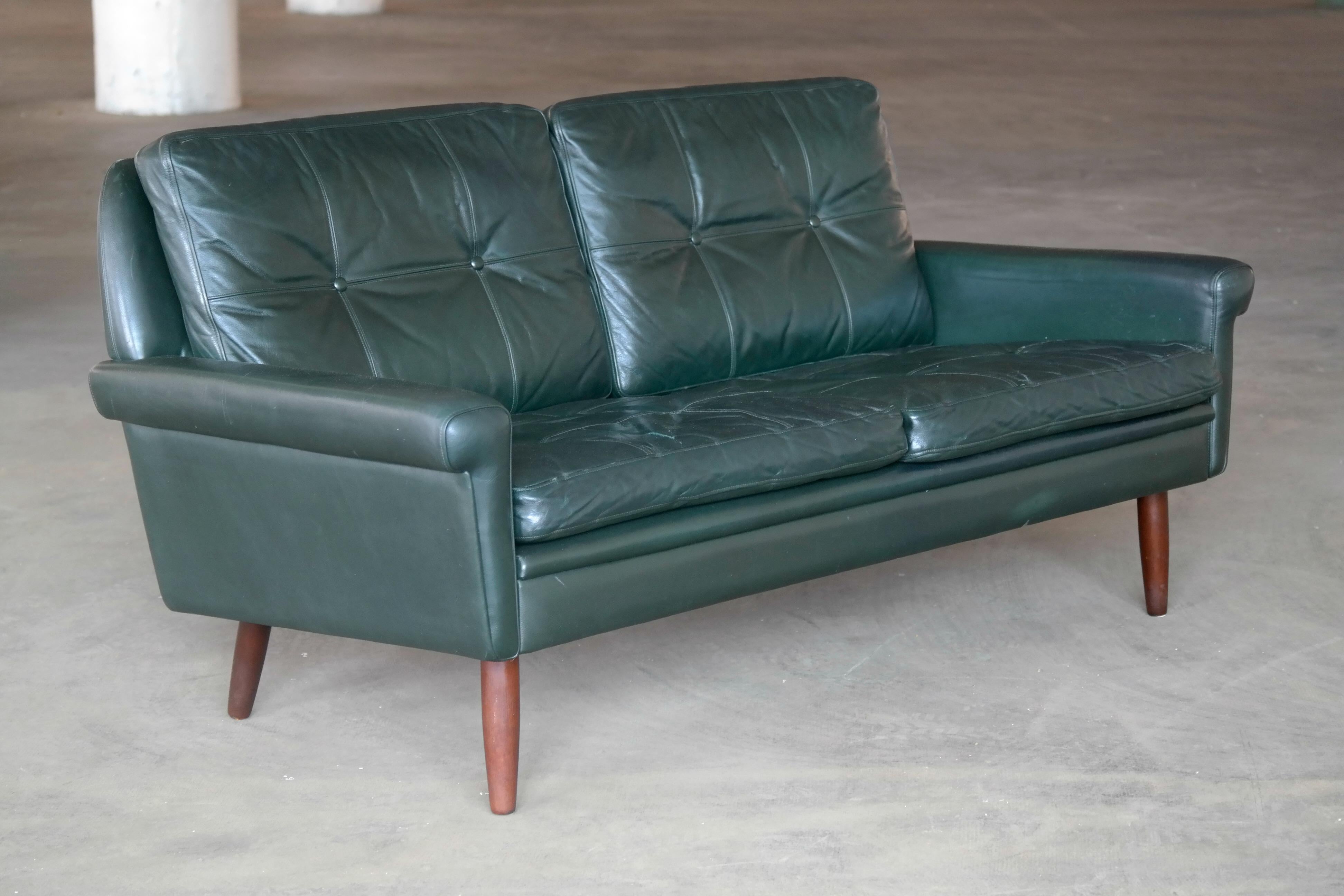 Wonderful loveseat or two-seat sofa designed by Sven Skipper in the 1960s. With loose cushions upholstered in buttoned leather in a dark racing green color raised on stained beech legs. Overall very good condition with some natural age wear and