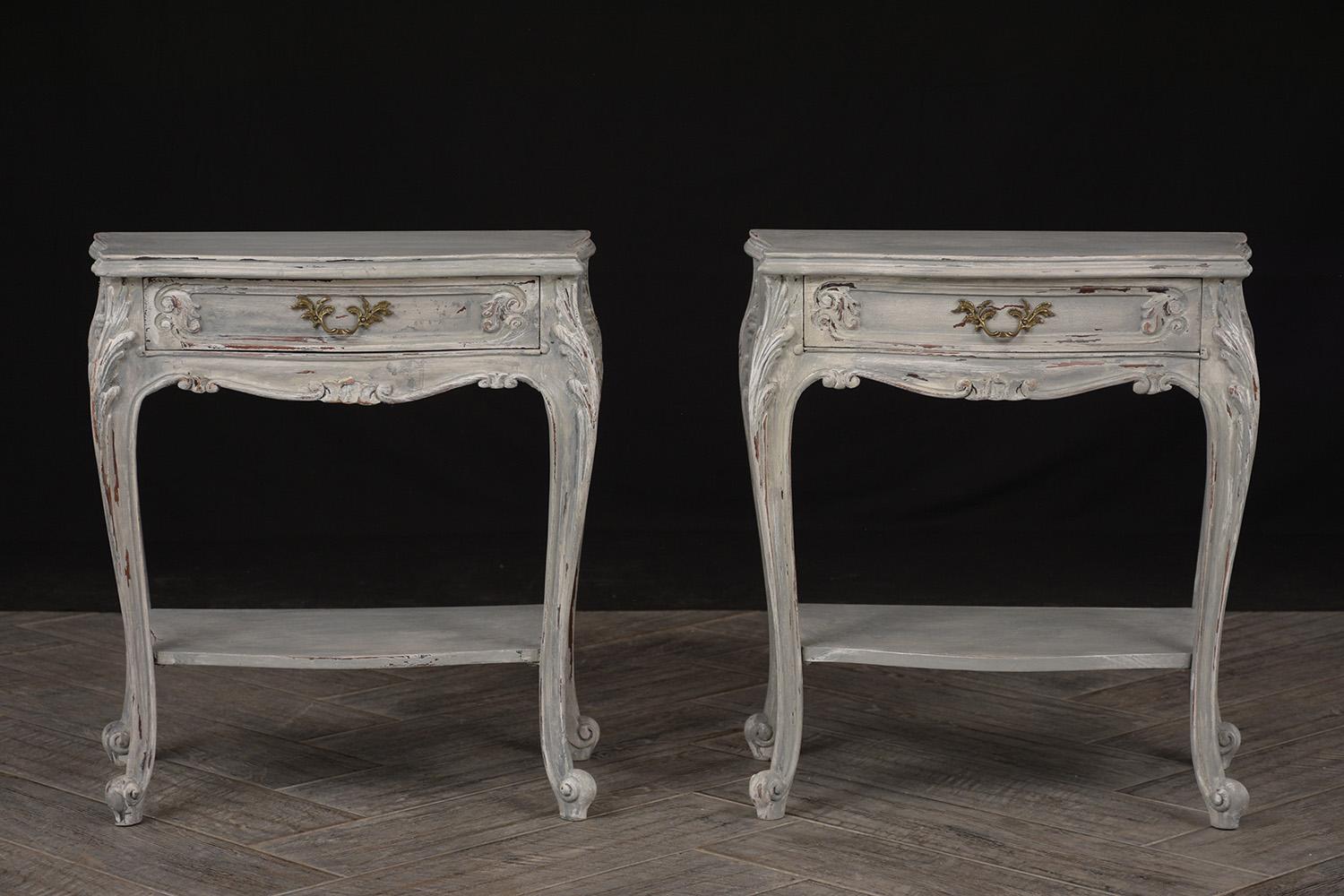 An elegant pair of 1970s end tables. Tables are made from solid mahogany wood and newly painted in a off-white and gray color combination with a lovely distressed finish. Features one single top drawer with brass design handle, one wood shelves at