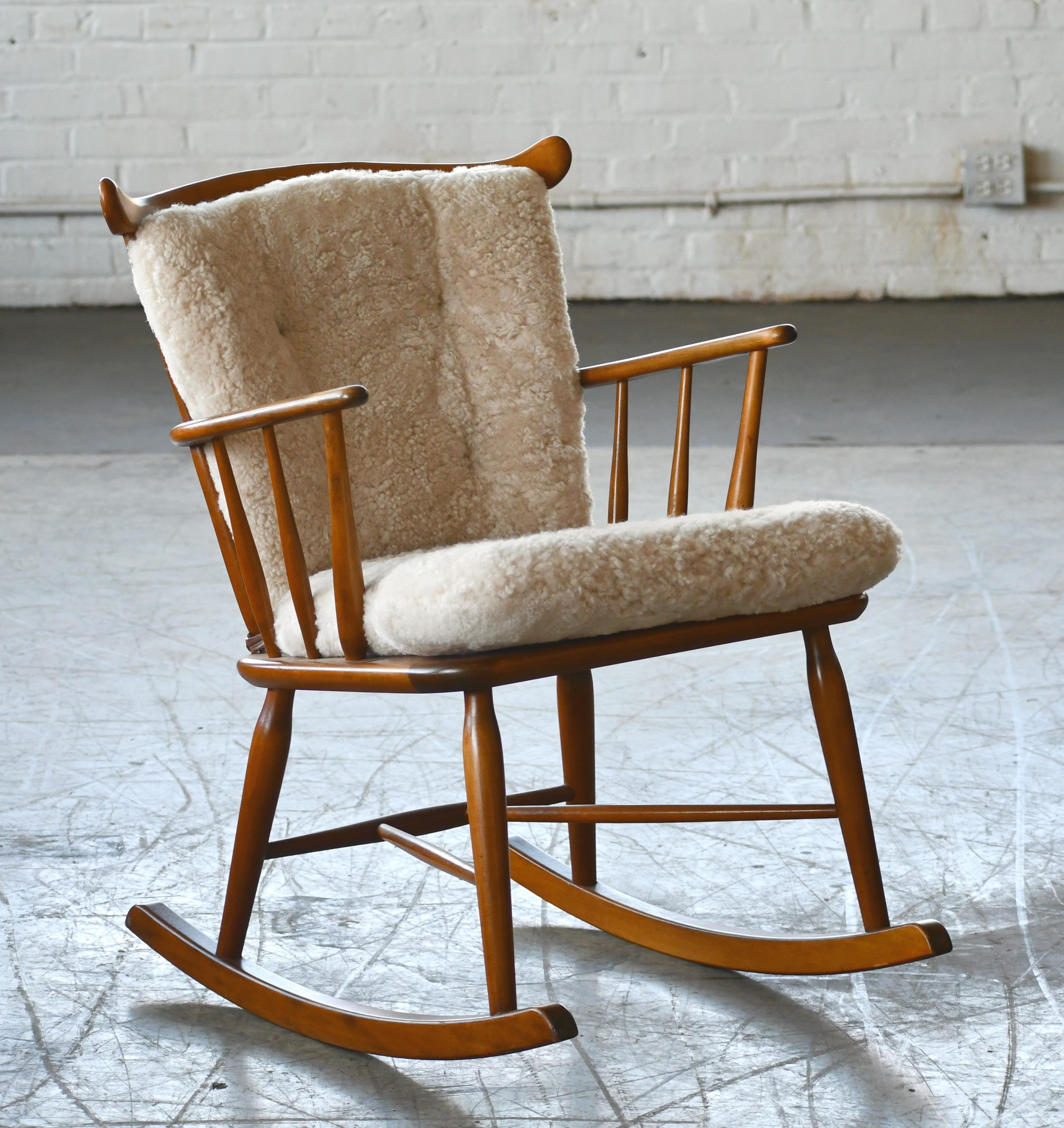Great little low back spindle back rocking chair from Faarstrup Mobler, Denmark made circa 1950. We re-upholstered the chair with new cushions in an exuberant curly sheepskin in a putty color and cognac colored leather buttons that just sucks you