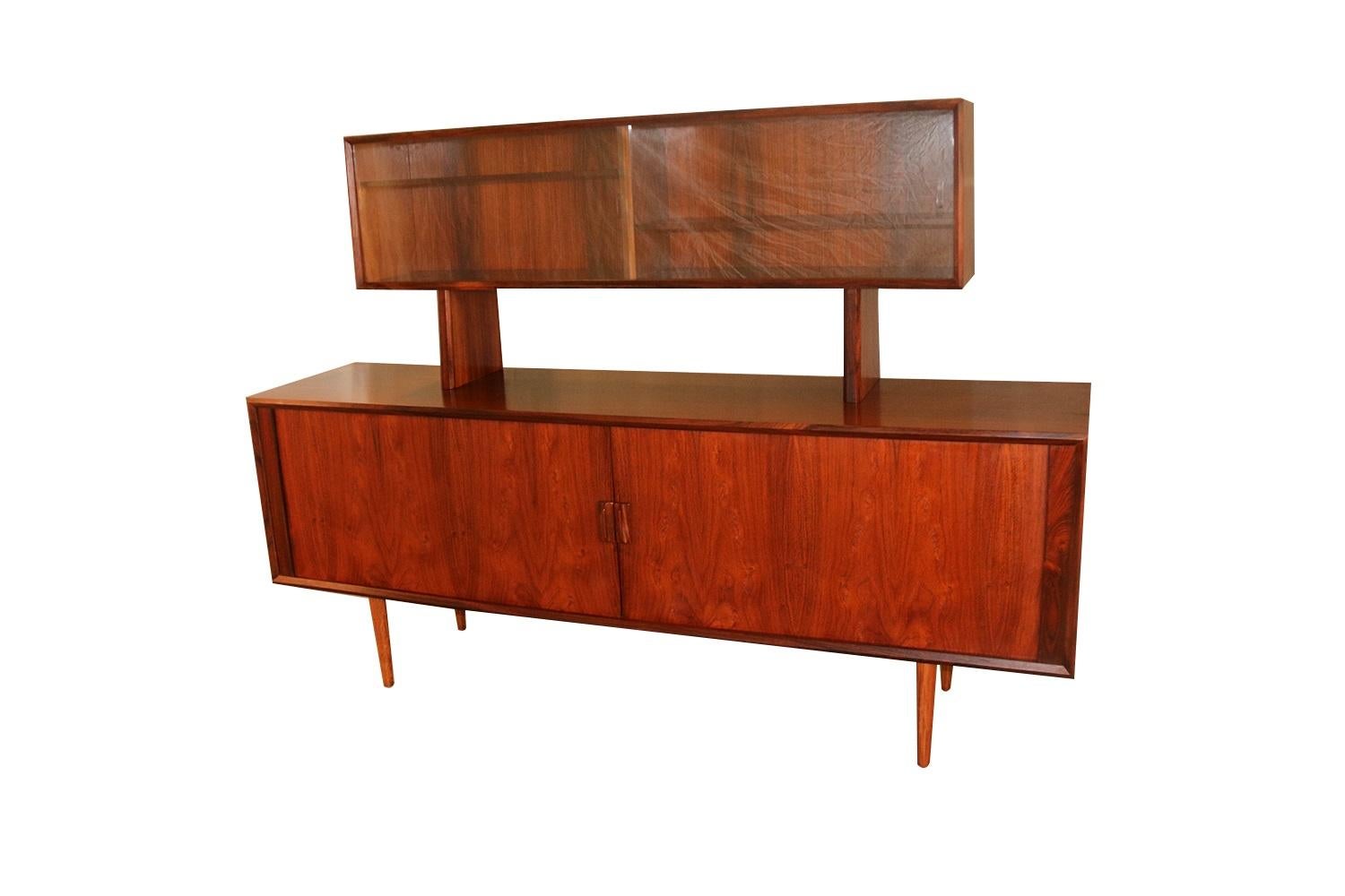 Remarkable rosewood, stunning two-piece hutch credenza by Famous designer Svend Larsen for Faarup Mobelfabrik made in Denmark. This Danish modern rosewood credenza, media China cabinet is beautifully embellished with bands of rosewood running