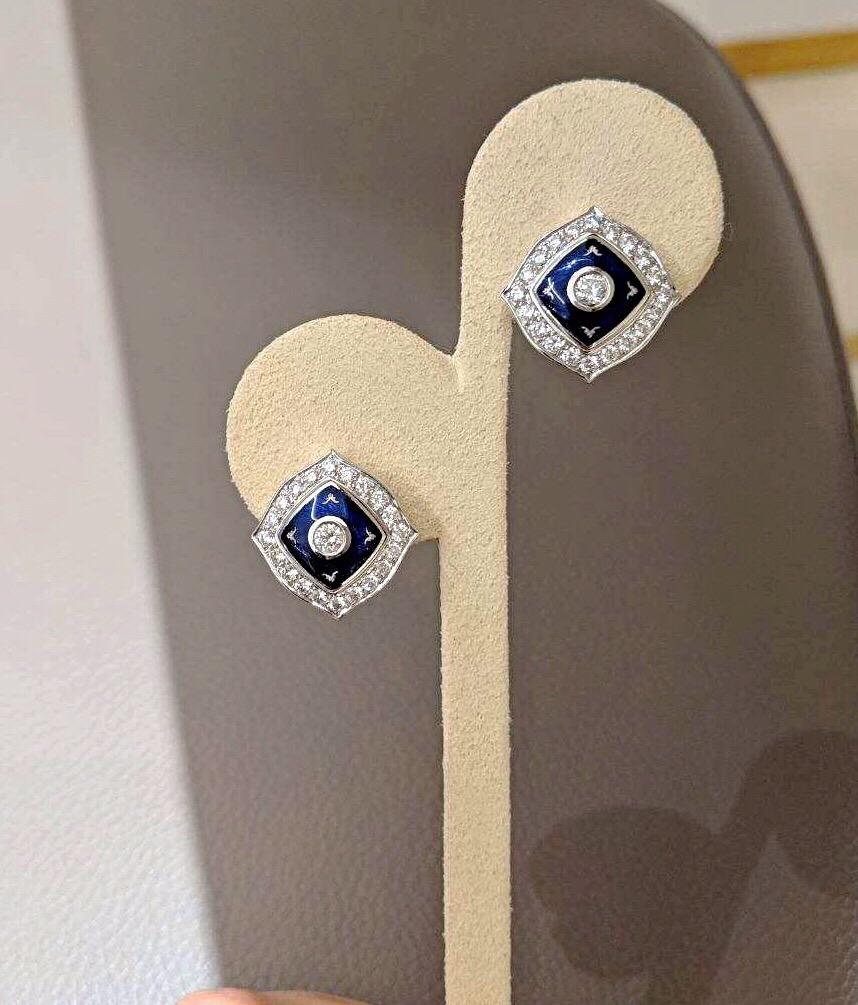 These  modern Faberge 18 karat white gold cushion shaped earrings center a bezel set round brilliant diamond. A raised square of Prussian Blue enamel surround the center diamond. Round brilliant white diamonds border the entire earring.
The earrings