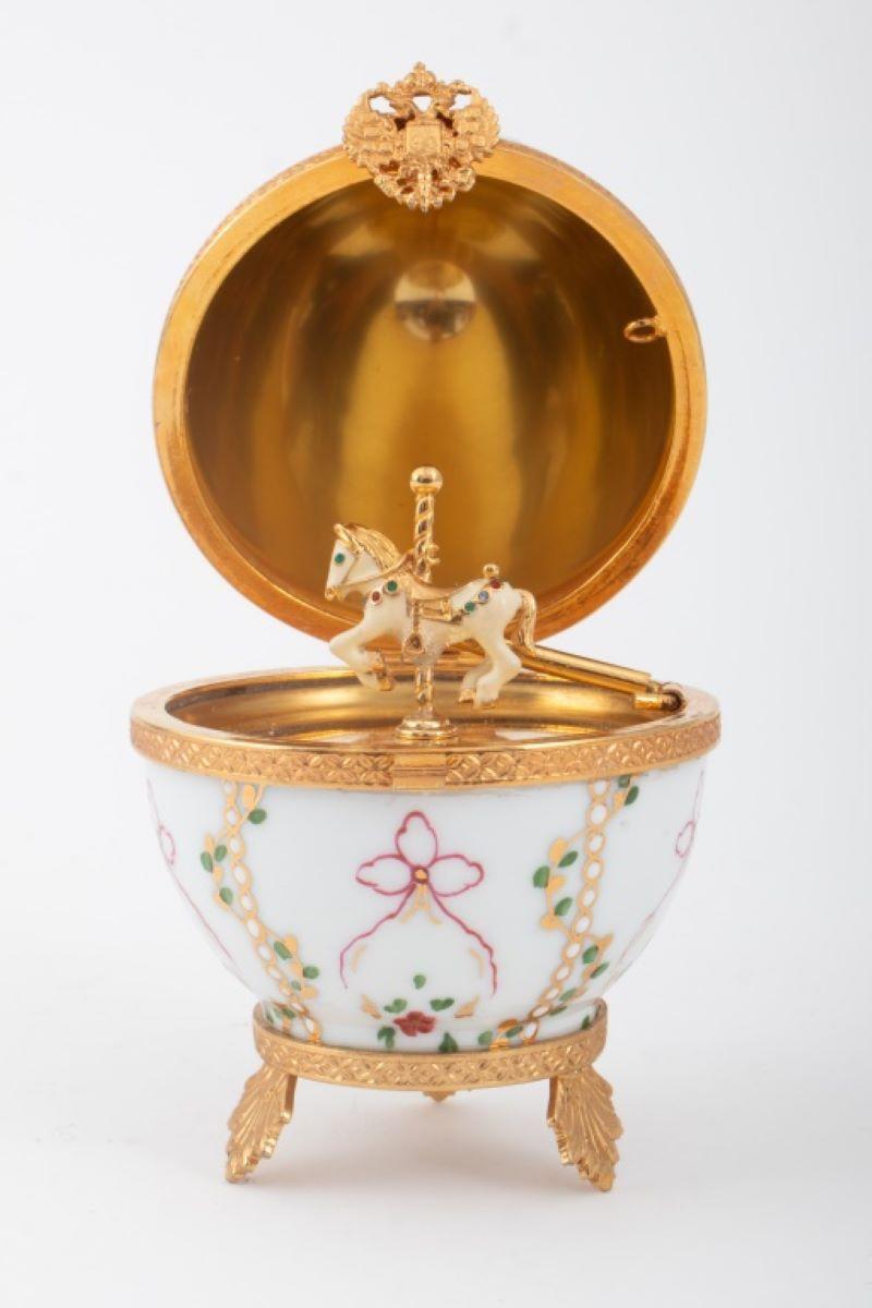 Faberge After Imperial Gatchina Palace Porcelain Egg, hand-painted with hanging bouquets and raised white enamel dots, interior gold-plated and with carousel horse with rhinestones on bridle, double-headed eagle crest clasp, peg to hold open, on