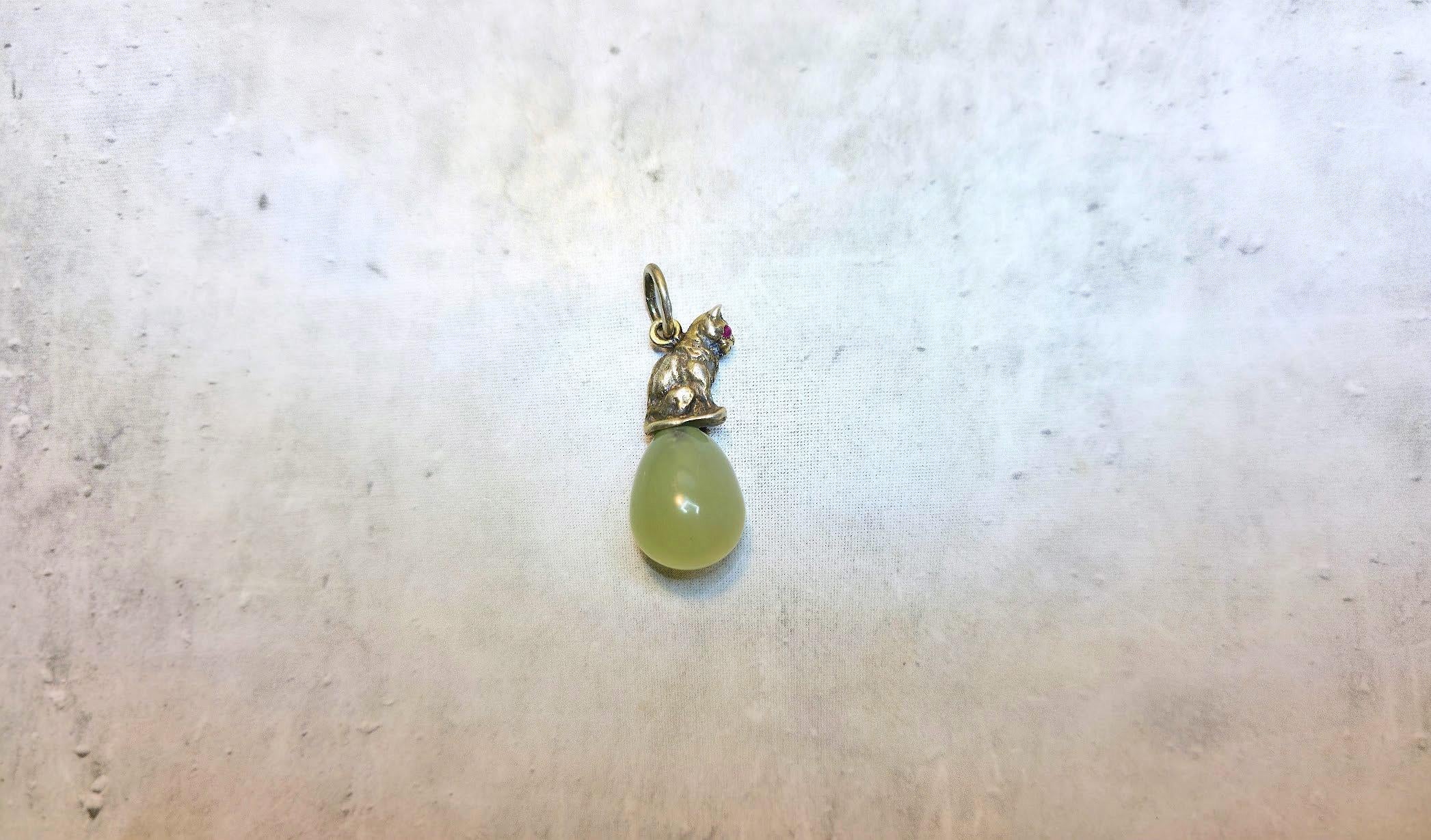 Nos complace presentar una pieza única y extraordinaria de nuestra colección: un colgante de huevo de bowenita con una figurita de gato de plata dorada con ojos de rubí, creada por el legendario maestro Julius Rappoport. 

El colgante está elaborado