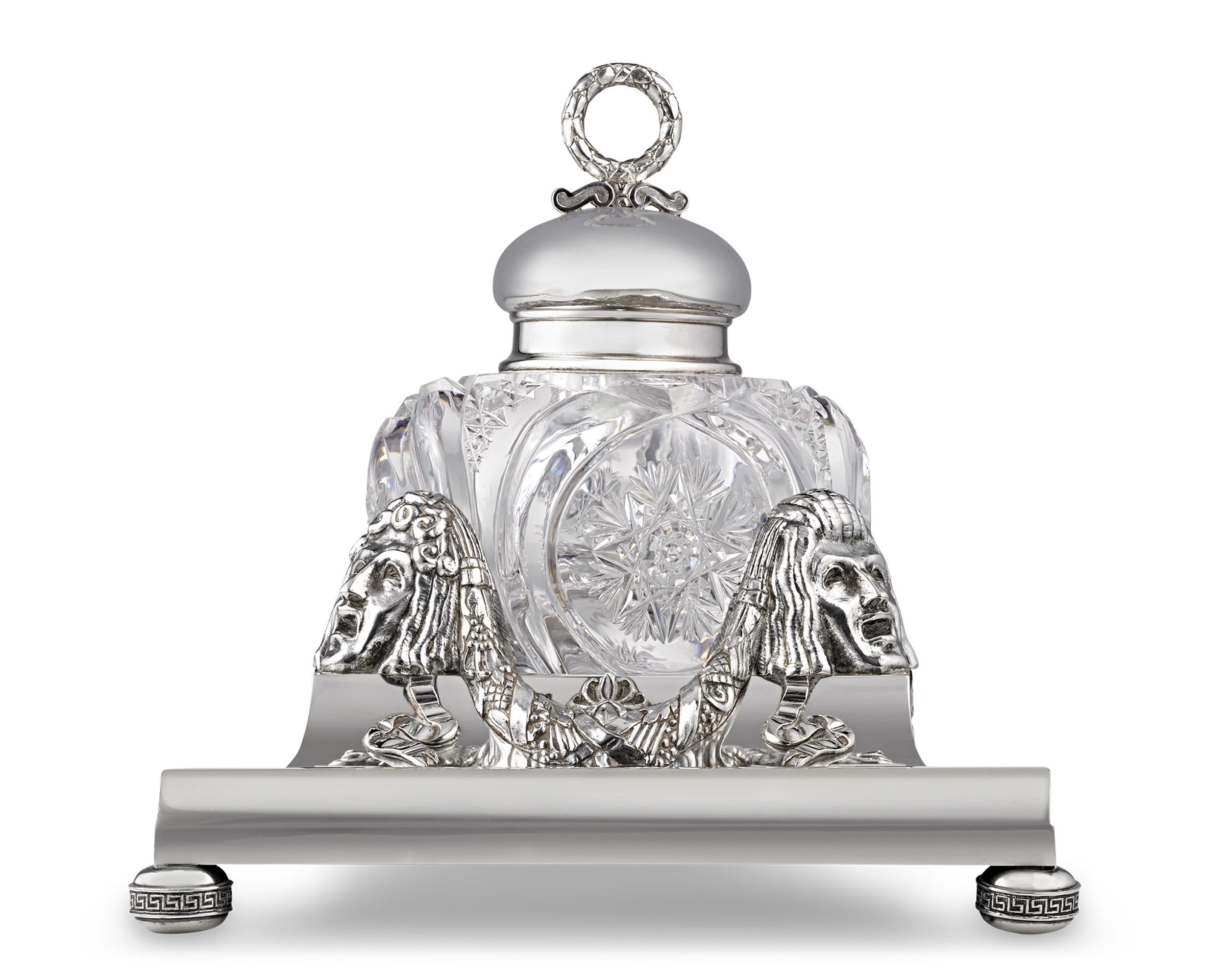 This exquisite inkwell by the legendary Fabergé exudes a bygone luxury. Comprised of intricately cut glass in a star pattern, the inkwell rests upon a silver base cast with dramatic masks among foliate festoons and ribbons. Its refined, neoclassical