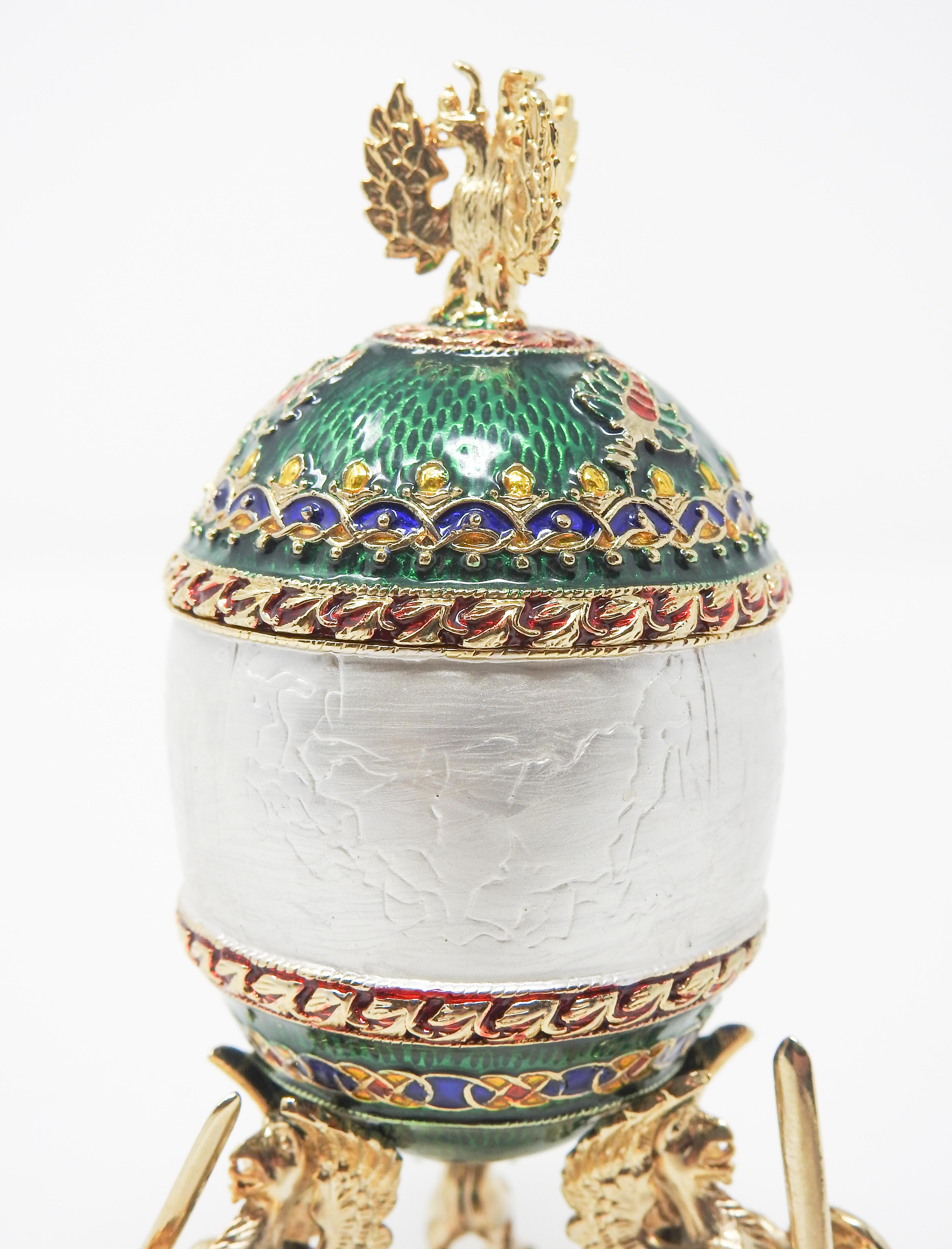 Offering this stunning Faberge style egg. Starting on a pearl enamel base with three winged figures. The egg sits atop the winged figures and is done in vibrant tones of green, silver, red, blue, yellow, and burgundy. There is Greek stamped on the