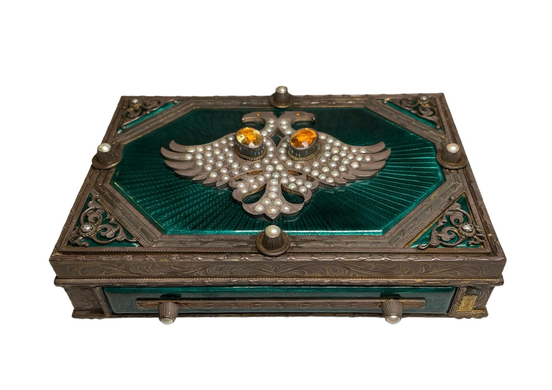 This is Faberge style rectangular patinated 925 silver metal decorative box/cigarette case. It depicts a heavy hinged box very well ornamented. The top of the lid is covered by an octagonal shaped emerald green translucent guilloche enamel in the