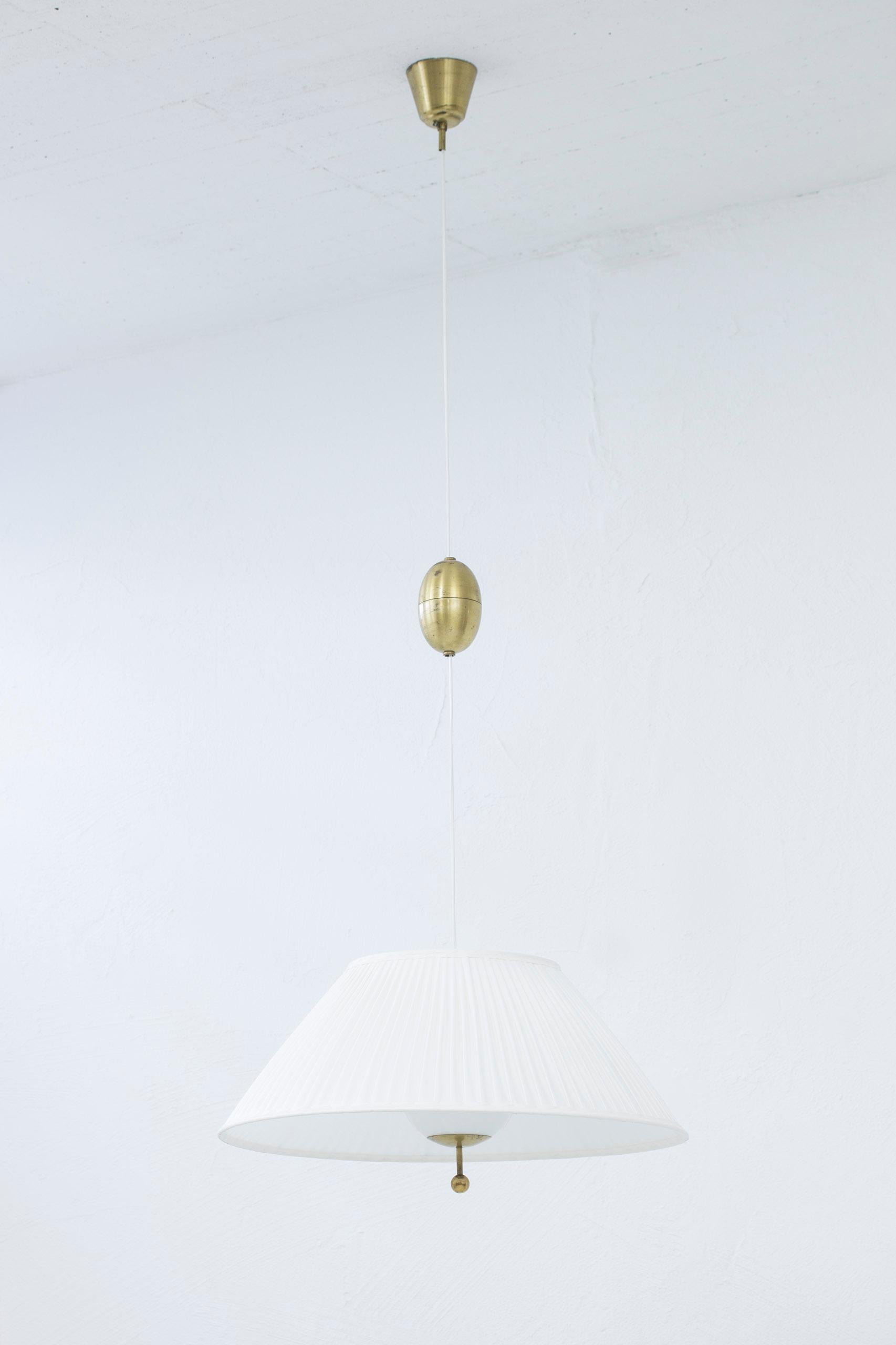 Ceiling lamp designed by Harald Notini. Produced in Sweden by Böhlmarks lampfabrik during the 1940s. Made from Opal glass with a hand pleated shade resting on the glass. Ceiling mount, pulley and grip all in brass. The lamp extends from 120-175 cm