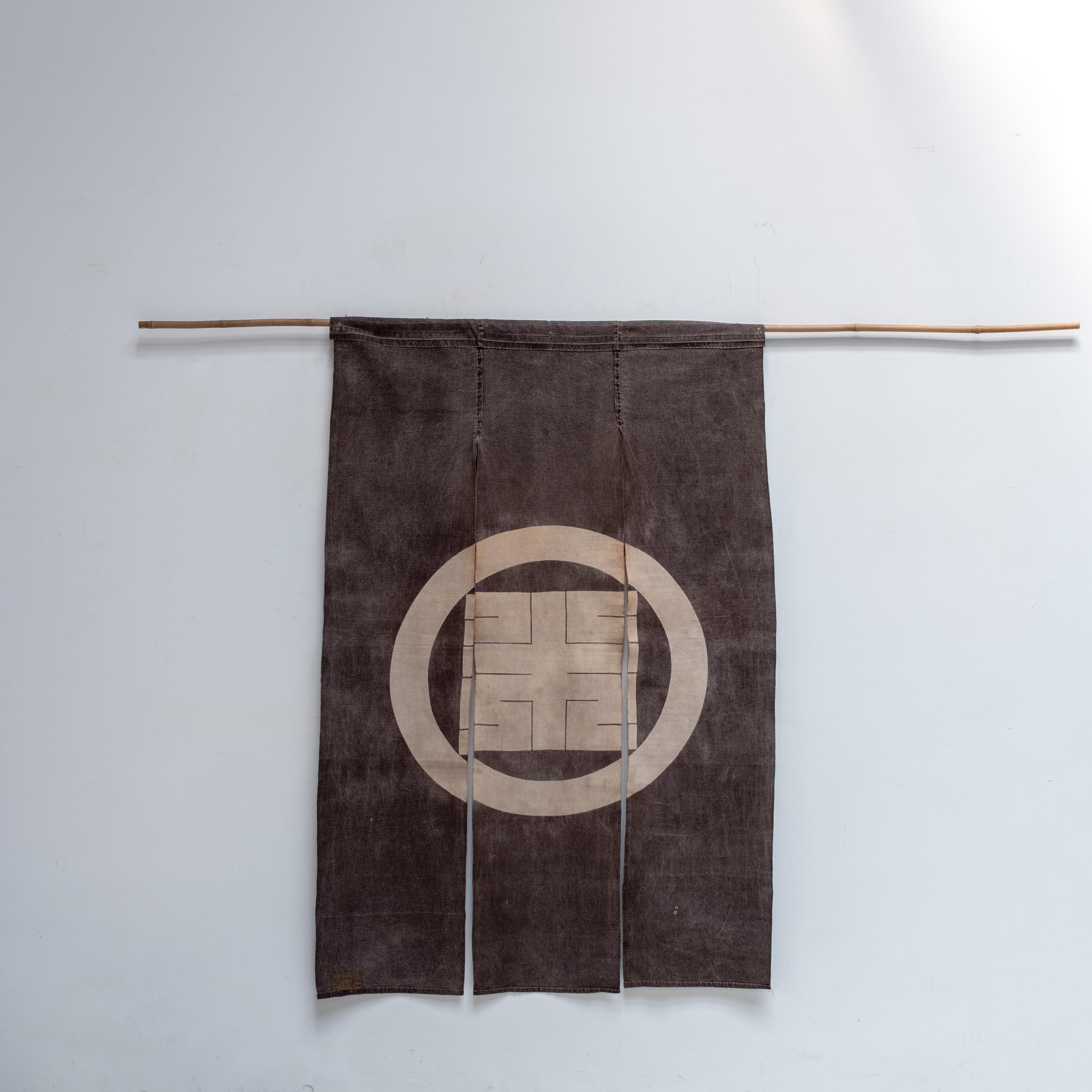 Se trata de un noren (cortina de tela para tiendas) tradicional japonés del periodo Taisho (1912-1926), elaborado con algodón teñido con tanino de caqui (kakishibu). Con el tiempo, el tinte se ha desteñido maravillosamente, creando una pátina cálida