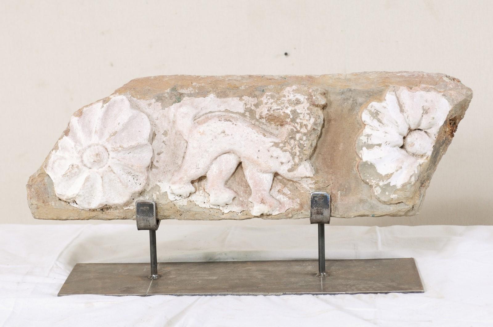 An exquisite 18th century Spanish carved-stone fragment, with mythological creature and flowers, on custom iron stand. This antique fragment from Spain features a horizontally set stone which has been hand carved with a mythological creature,
