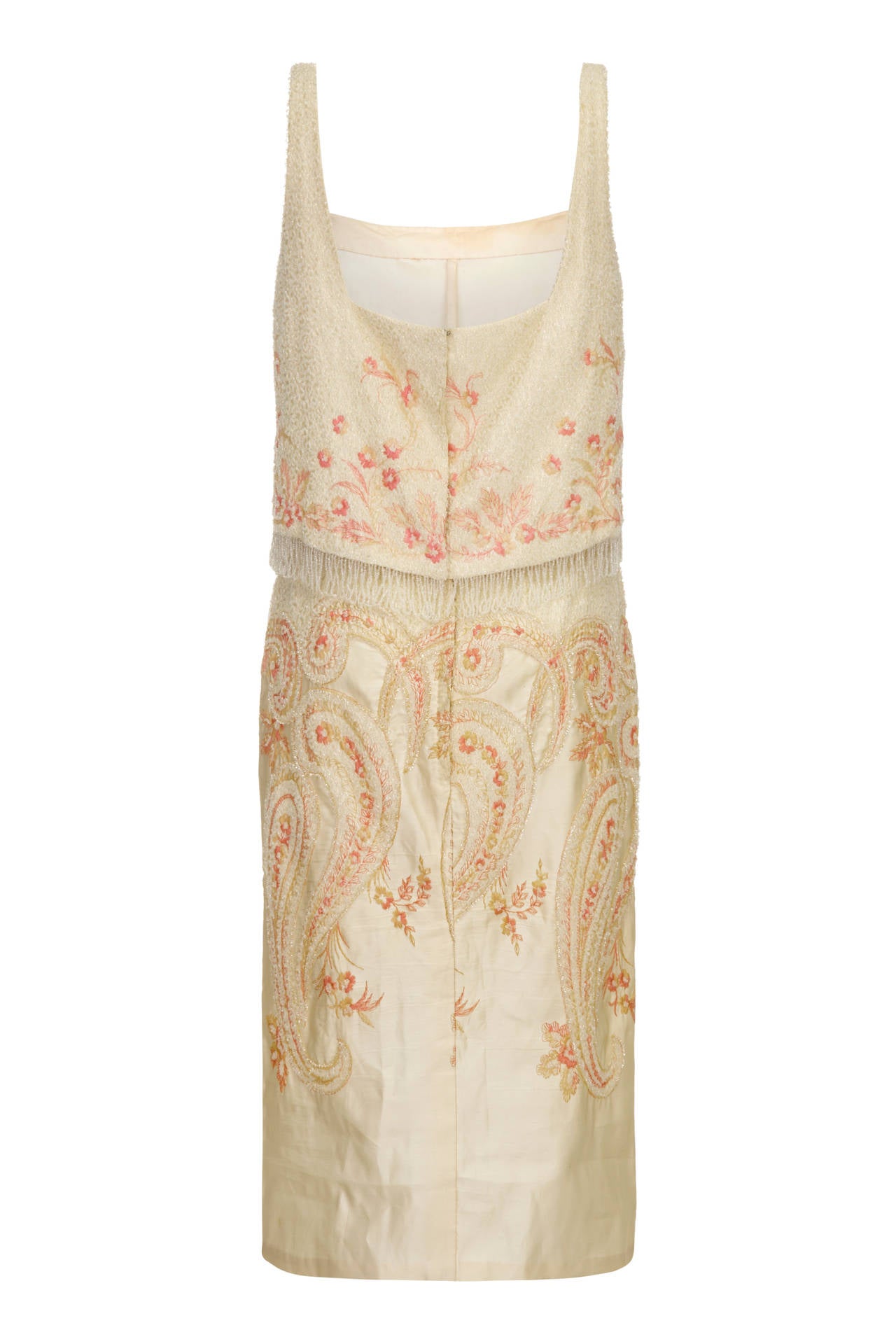 This exquisite 1960s cream and peach toned silk cocktail dress is heavily embellished with tiny rocaille beading and is in superb vintage condition. The bodice is embellished in its entirety and elevated over the waistline with a beaded tassel