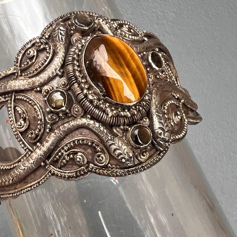 Exquisite vintage Straits Chinese cuff bracelet, likely crafted in Bali, is a stunning example of skilled silversmithing from the early to mid-20th century. The bracelet features meticulous craftsmanship with intricate Etruscan-style wirework and