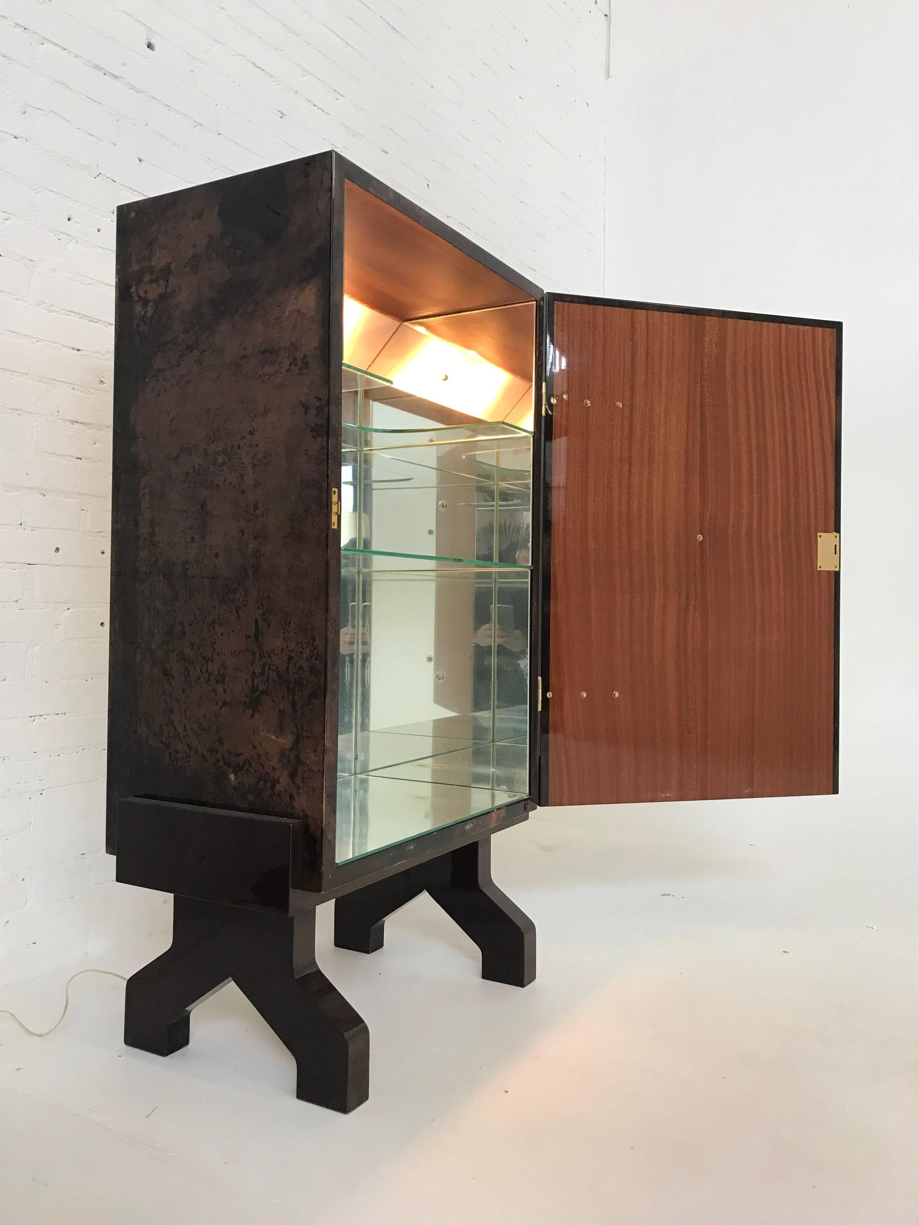 Two-door brown Goatskin dry-bar cabinet with brass studs and hardware on separate wood stand. Mirrored, lighted interior with glass shelves. Exceptional designer piece made in the 1960s.