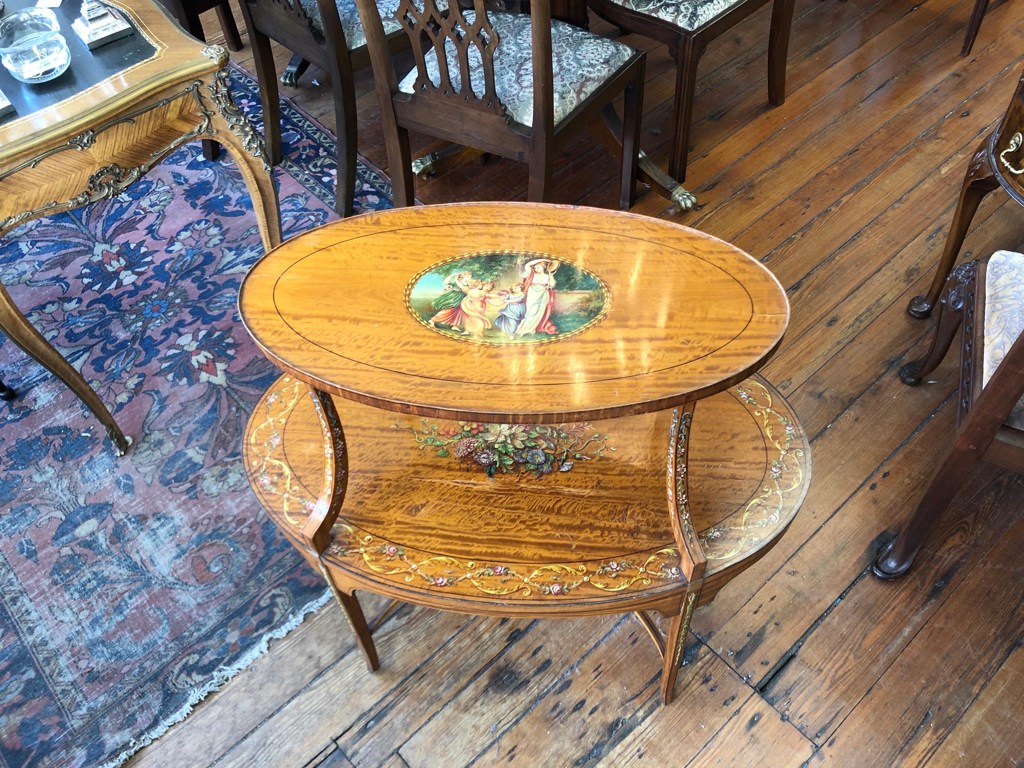 Se trata de una fabulosa Mesa de Postre o de Servir de dos pisos, ovalada, estilo Adam, inglesa antigua, pintada a mano y con incrustaciones. El cuadro está excepcionalmente bien hecho por artistas que probablemente pintaron muebles además de sobre