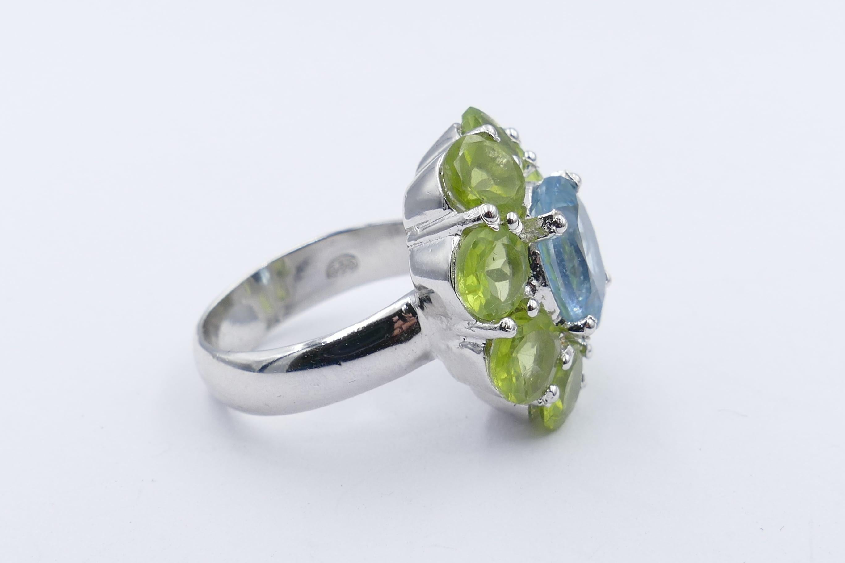 A stunningly cerulean blue is the colour of the 4.15 carat Topaz which forms the centrepiece of this Sterling Silver Ring. 
It is surrounded by 8 clear, light to mid green Peridots of excellent clarity, weighing 8.79 carats.
This very attractive